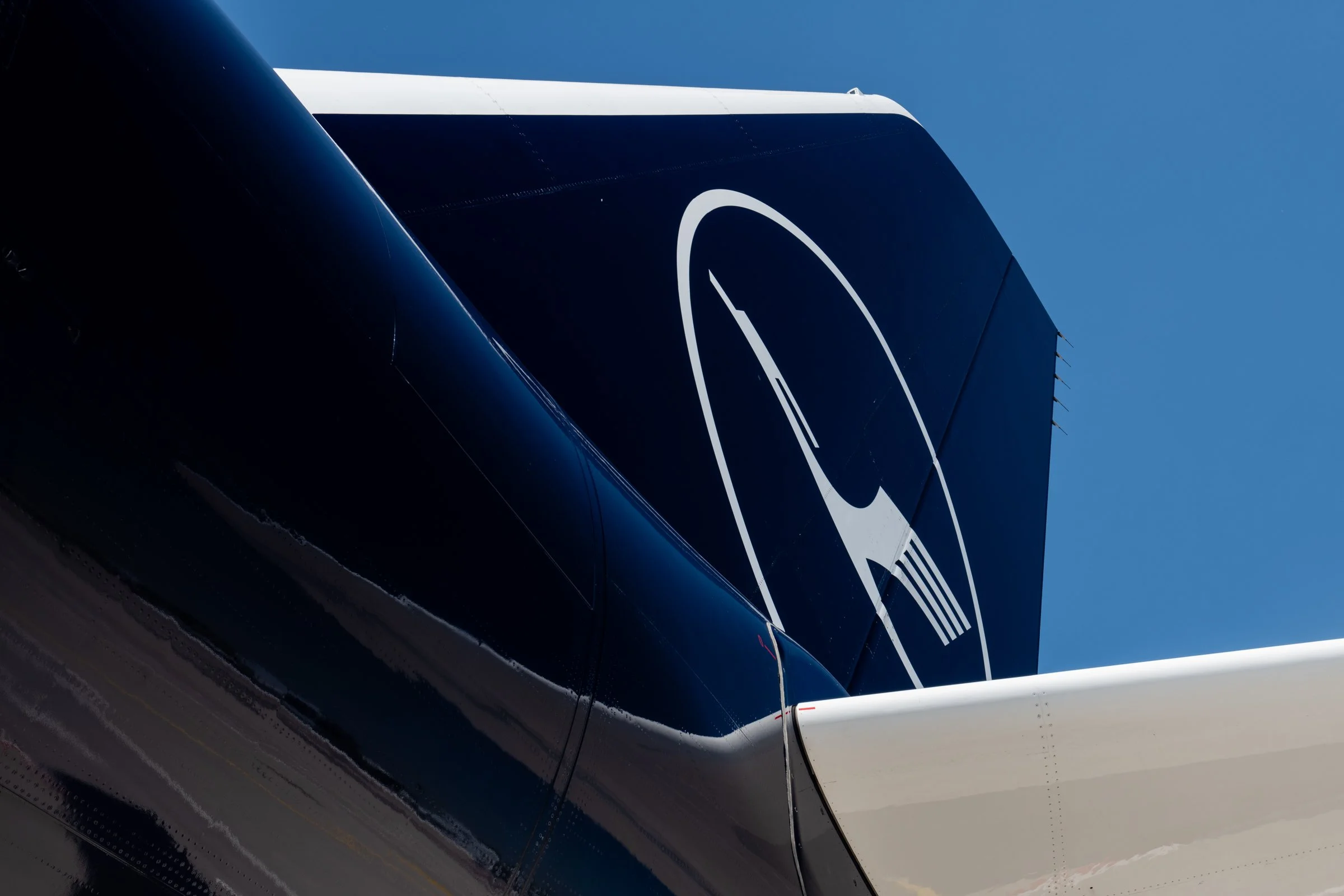 Close-up of a black vehicle with a white logo and white accents, taken from below against a clear blue sky.