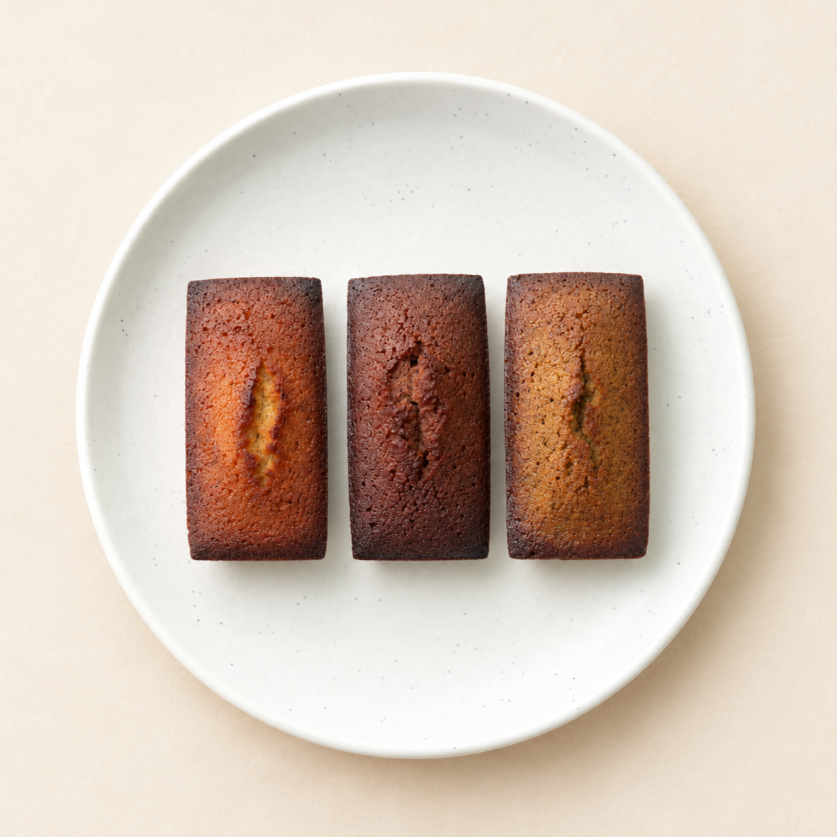 Three individual golden-brown baked cakes on a white round plate with a light background.