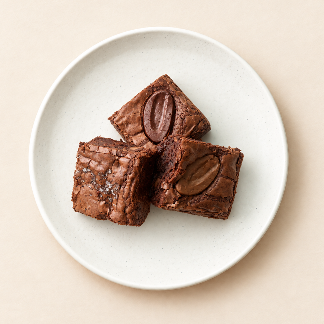 Three chocolate brownies with whole almonds on top, on a white plate