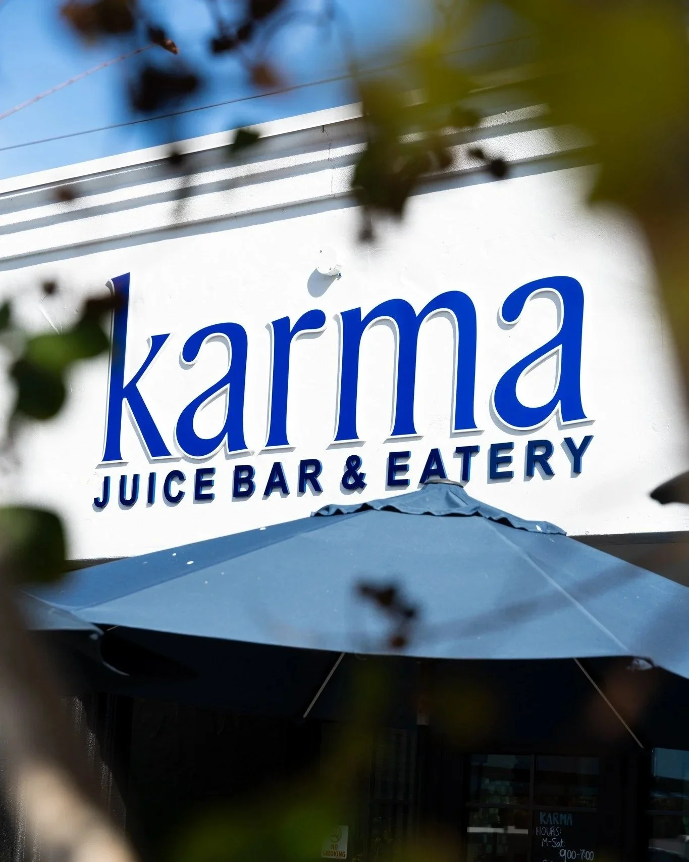 Sign for Karma Juice Bar & Eatery, seen through branches and leaves.