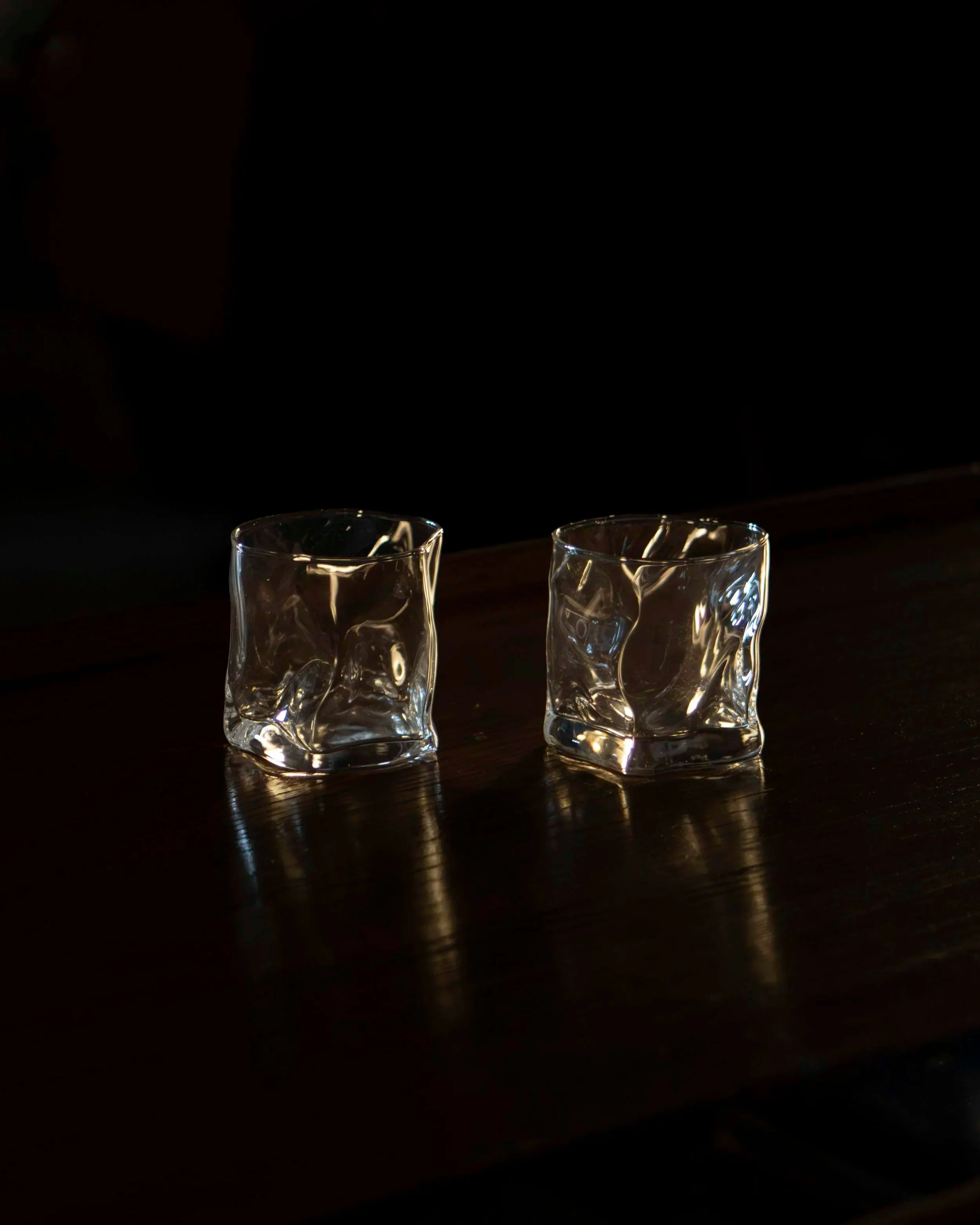 Two clear glass tumblers placed on a dark wooden surface with a black background.