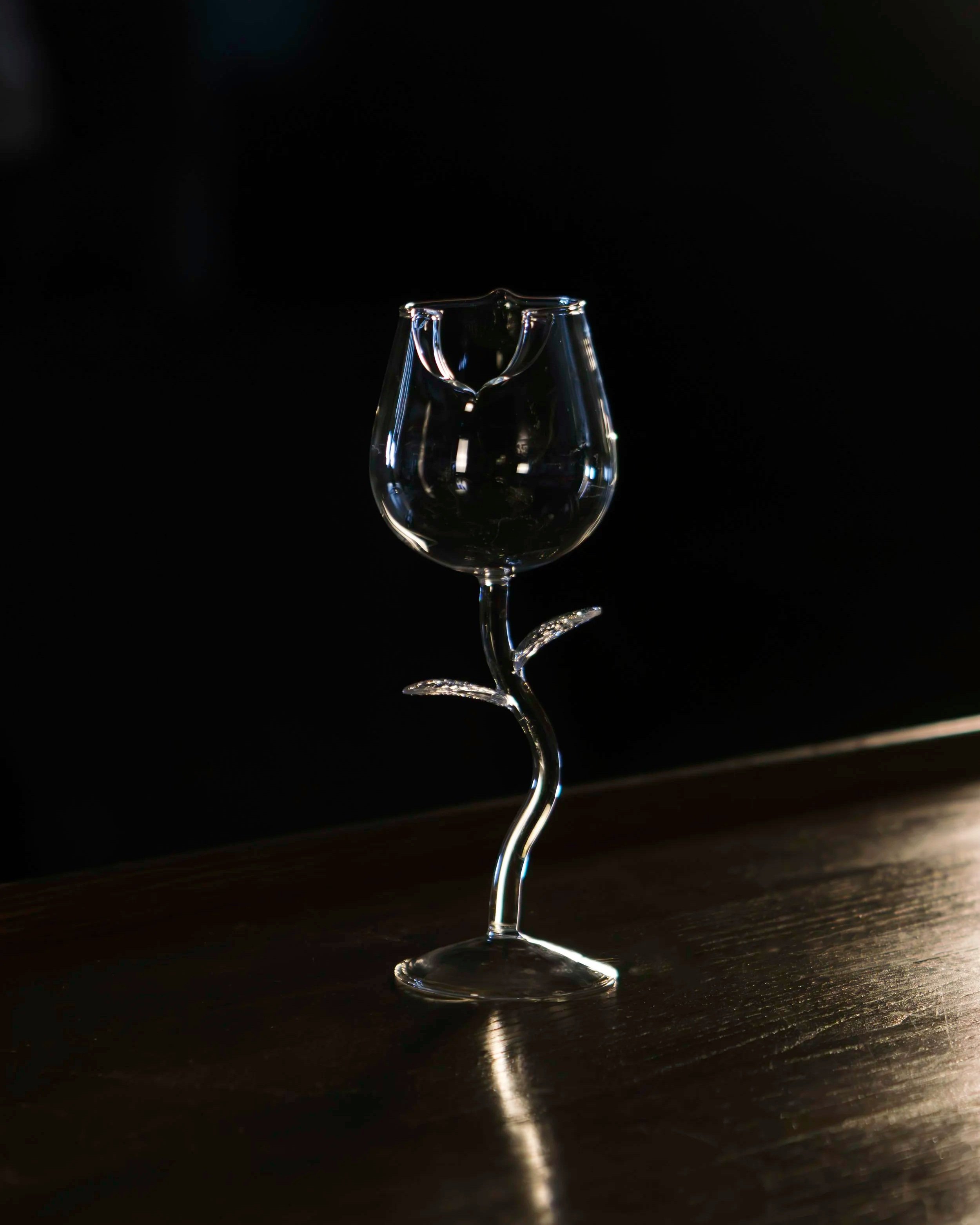 A clear glass with a candle holder on top, placed on a dark surface against a black background.