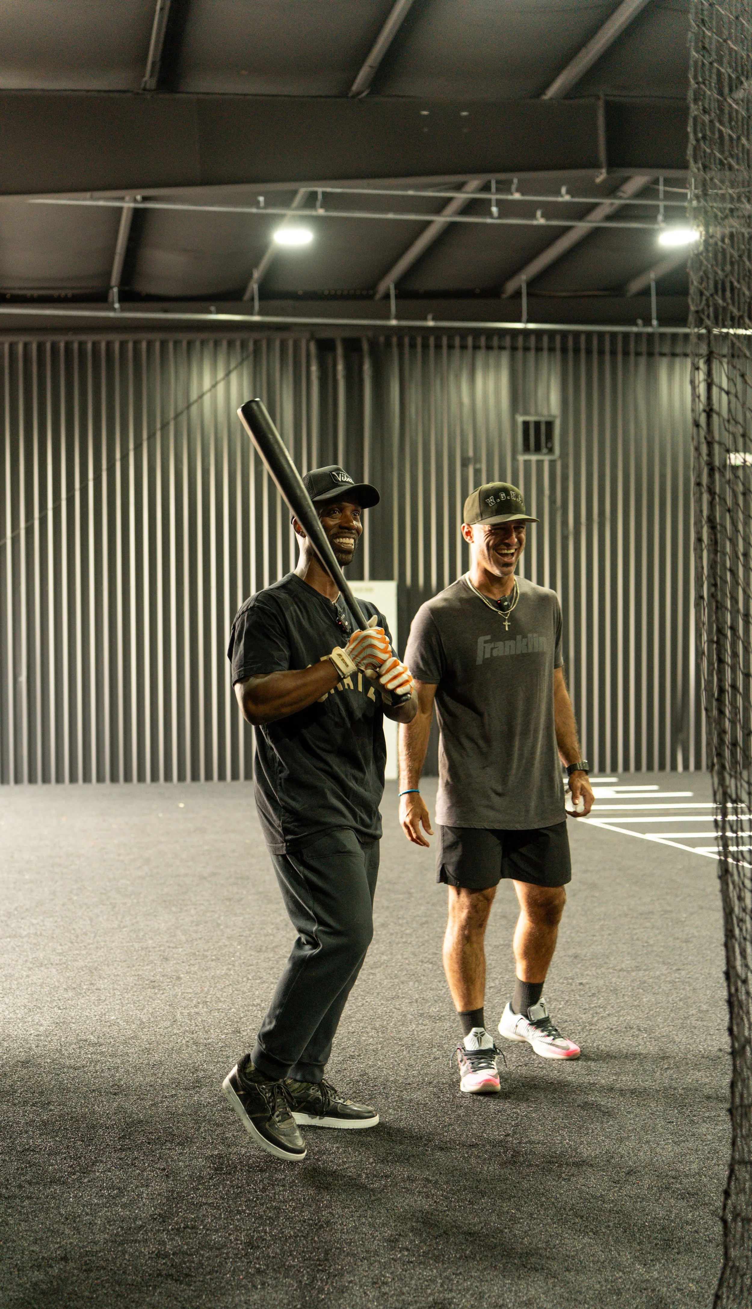 Andrew McCutchen and Sean Rodriguez inside The Yard baseball facility in St Pete, Florida. 

Two men smiling and holding a baseball bat, wearing athletic clothing and sneakers, behind a net and against a dark, industrial-style wall.