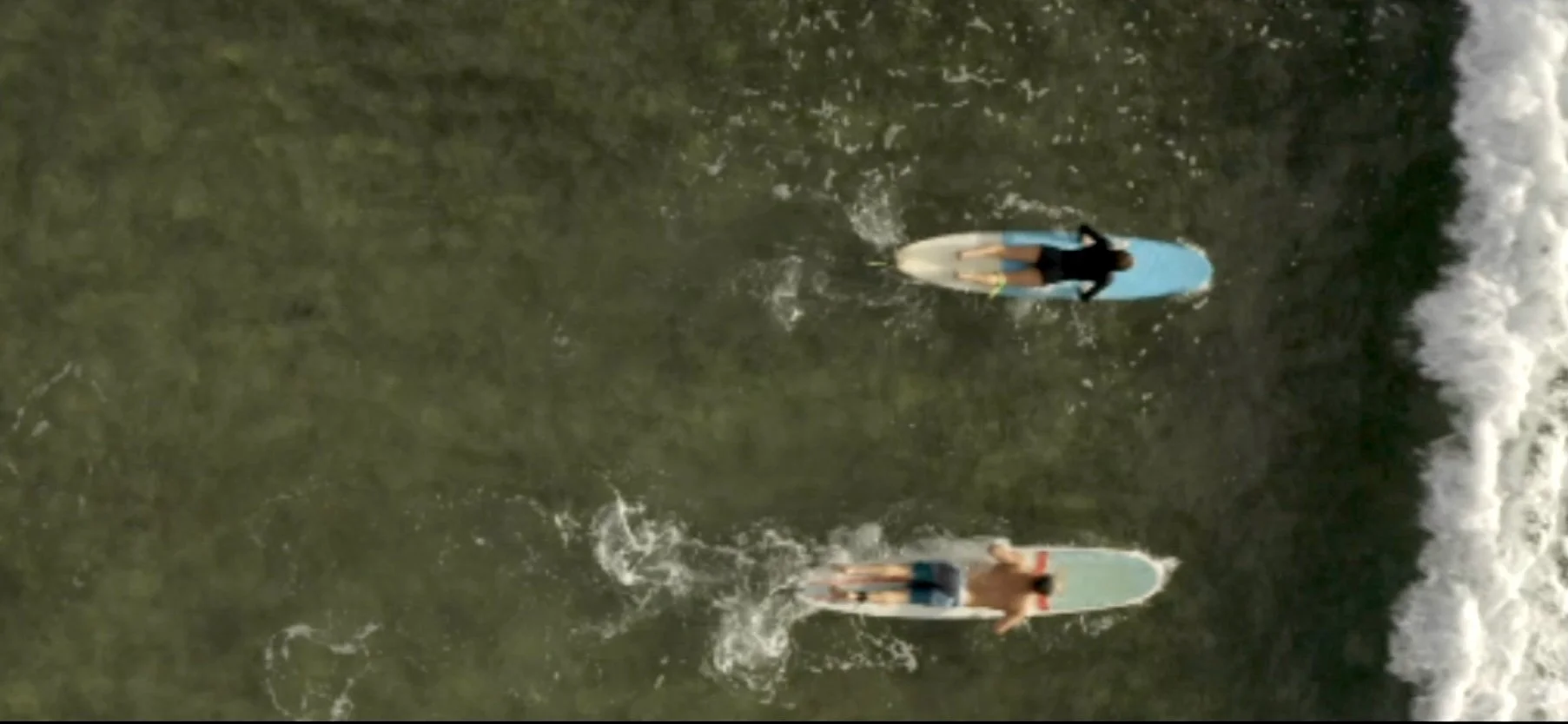 Two surfers paddling on their surfboards in the ocean near the shoreline.