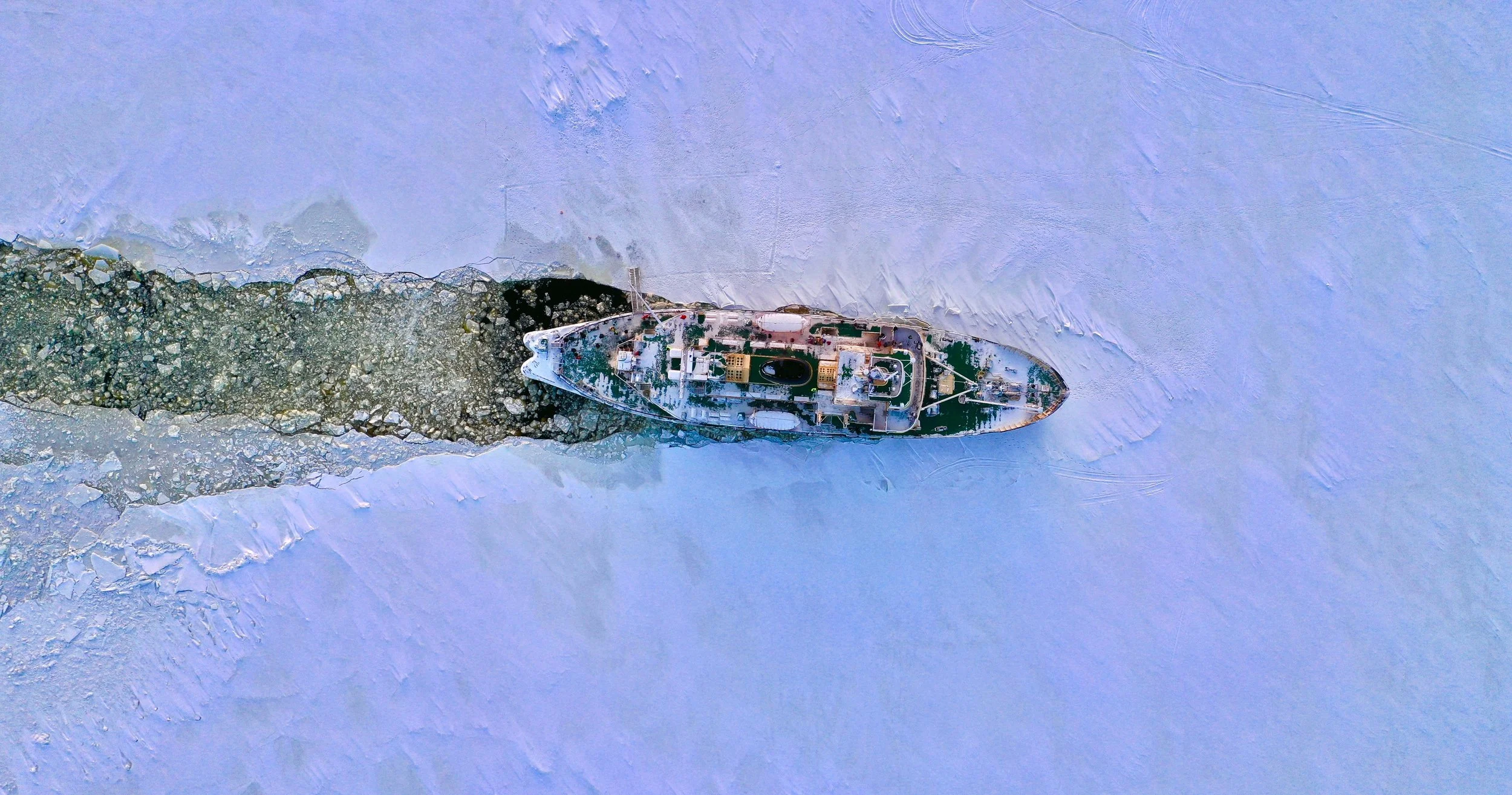 A ship navigating through icy waters with a trail of broken ice and snow behind it.