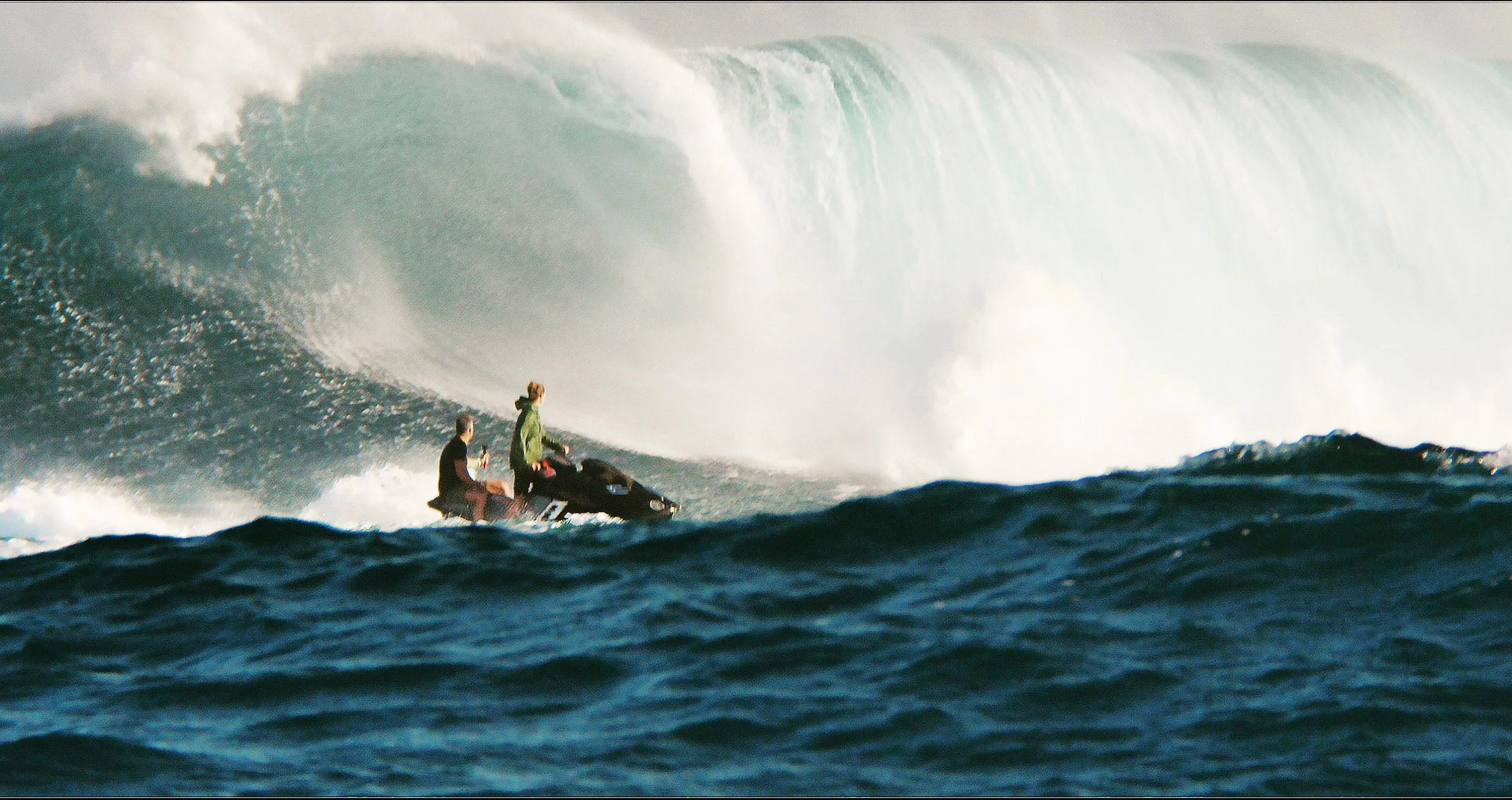 Two people riding a jet ski on the ocean near a large wave.