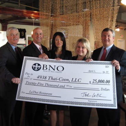 Group of five people holding a large check for $25,000 made out to Thai-Coon, LLC, from the Bank of New Orleans