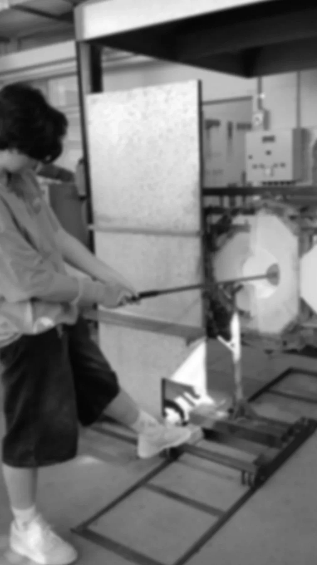 A person wearing a mask and gloves is operating a table saw in a workshop, cutting a piece of material.