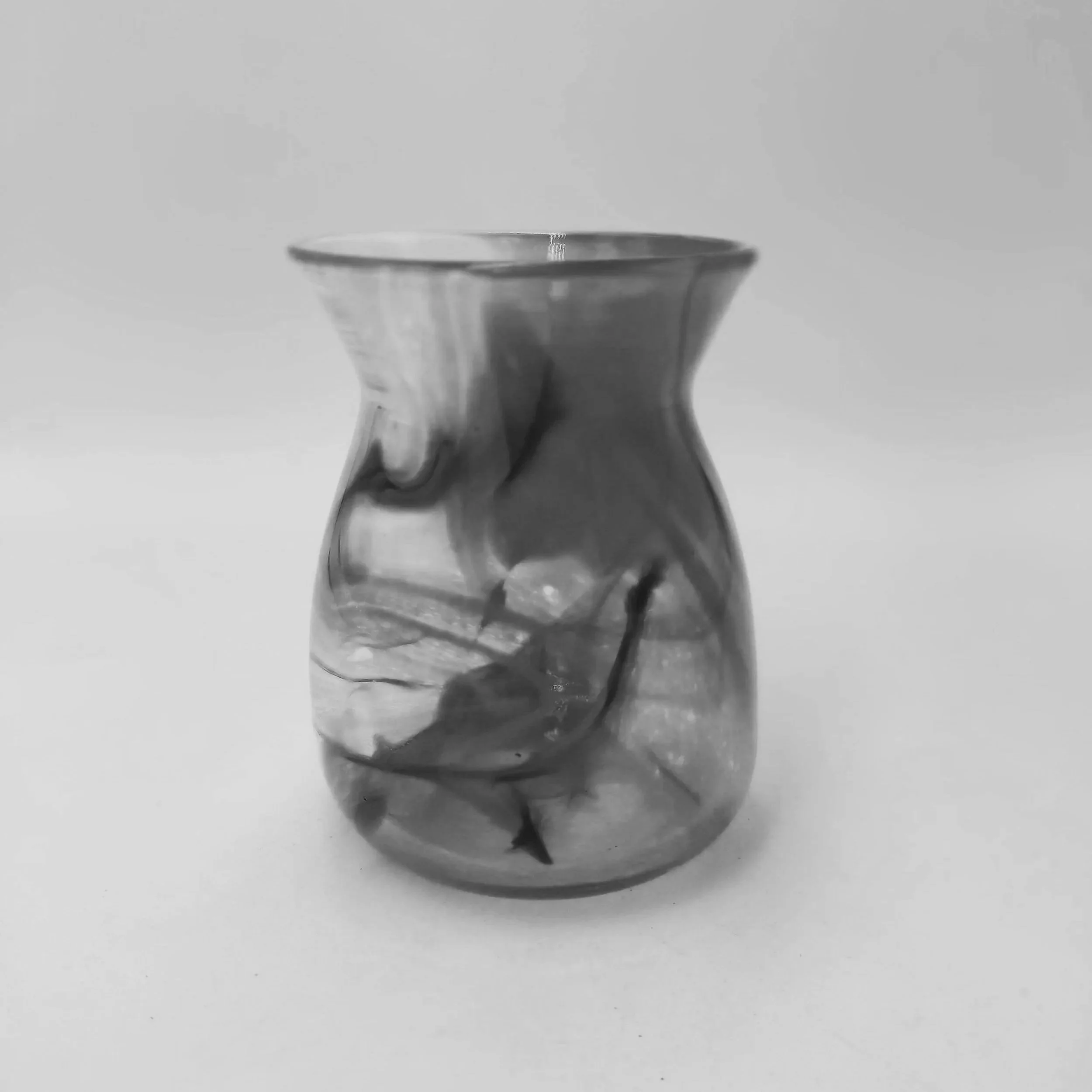 A black and white image of a glass or vase with a narrow neck and broad opening, set against a plain background.