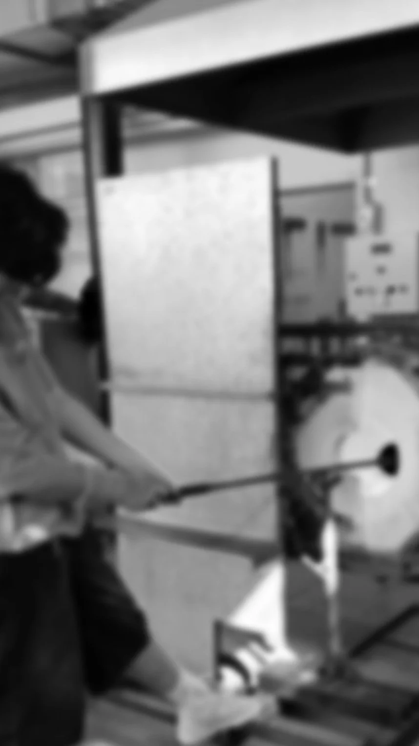 A person is in the process of Hot-Sculpting Glass, the glass is on the end of a iron inside the Reheating Chamber (Glory Hole) before shaping.