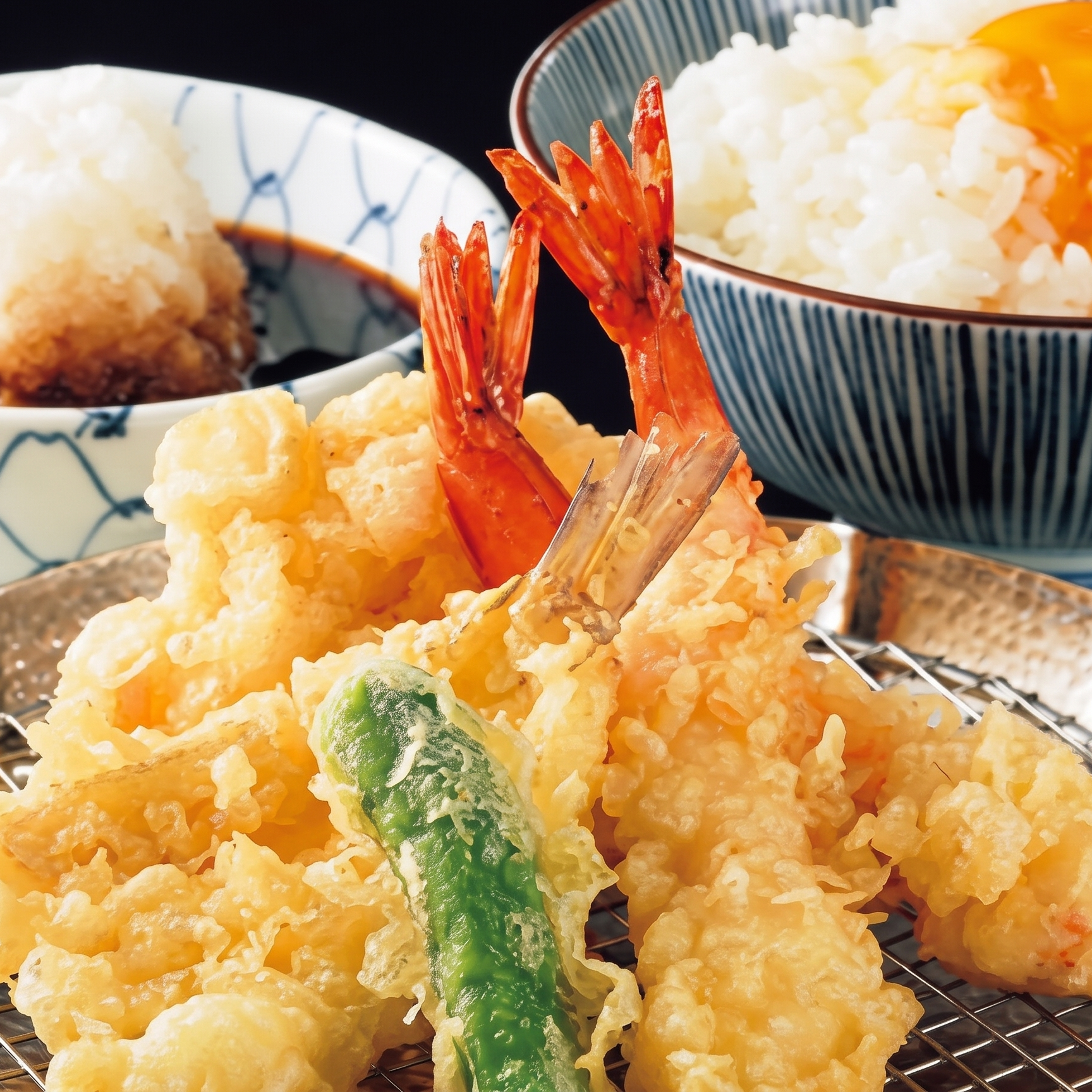 Close-up of assorted Japanese tempura including shrimp, vegetables, and rice in bowls.