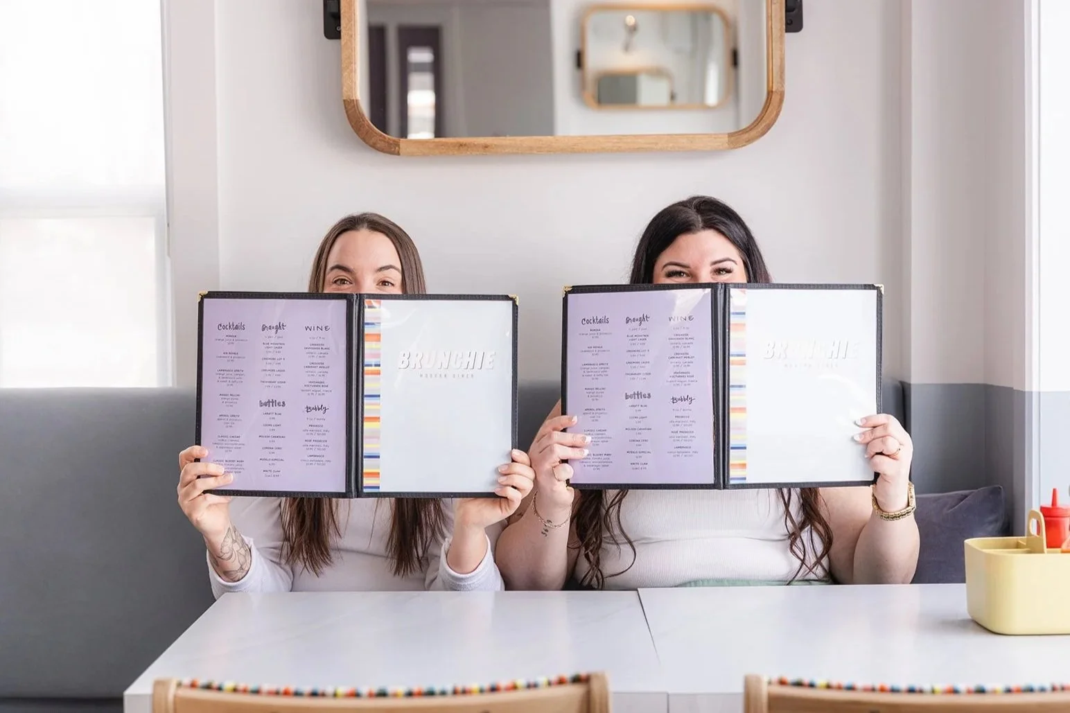 Two young women peeking out over open menus