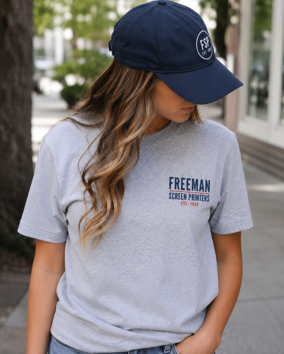 Woman wearing a branded T-shirt and hat while walking on a city sidewalk.