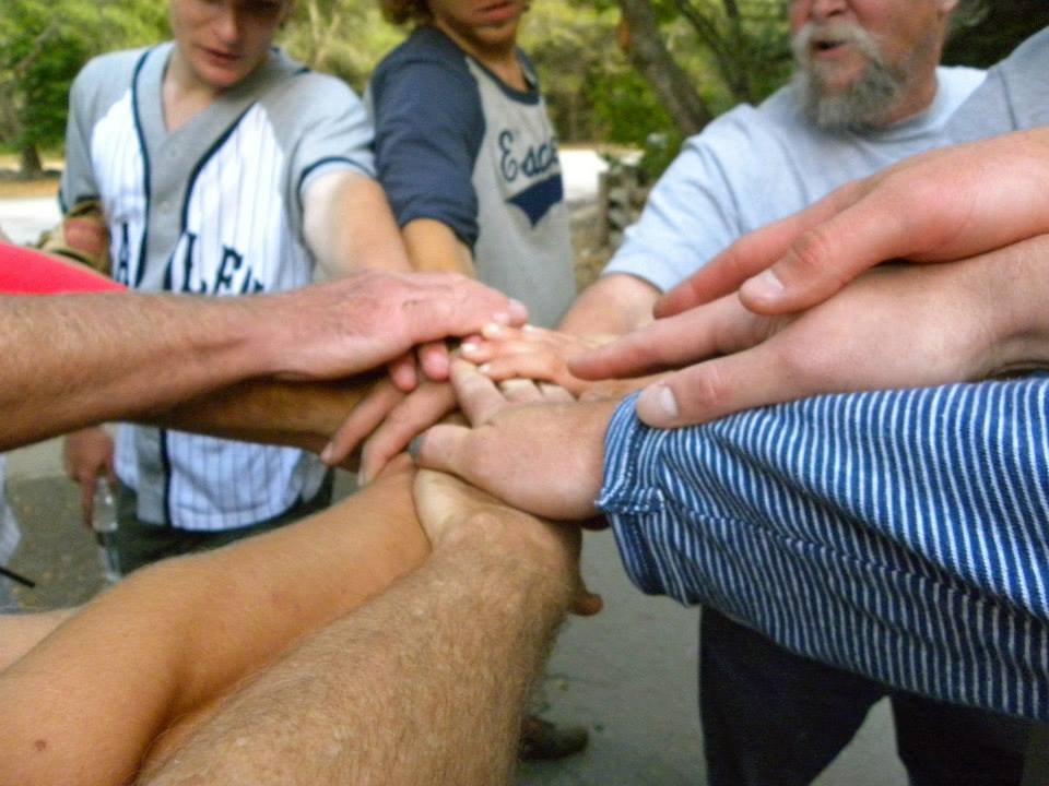 Multiple people are placing their hands together in a show of unity outdoors.