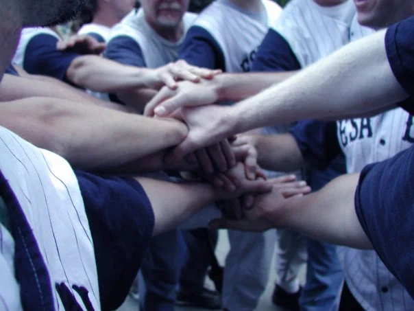 Baseball players in team uniforms stacking their hands together in a huddle.