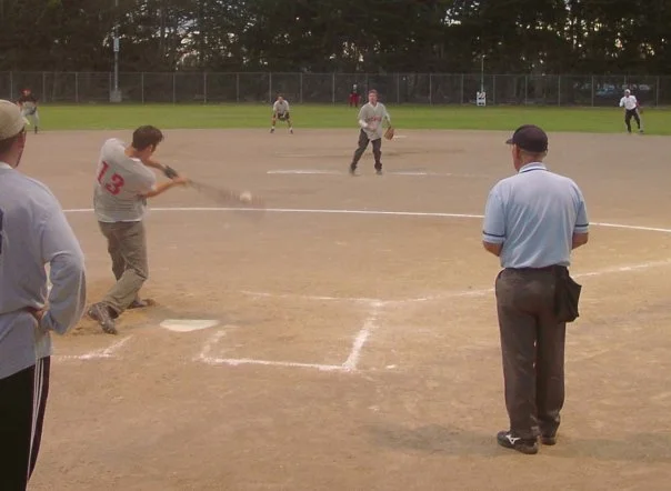 People playing baseball on a field with a coach and spectators watching.