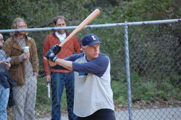 Person in baseball batting stance with a bat on a baseball field, with spectators in the background.