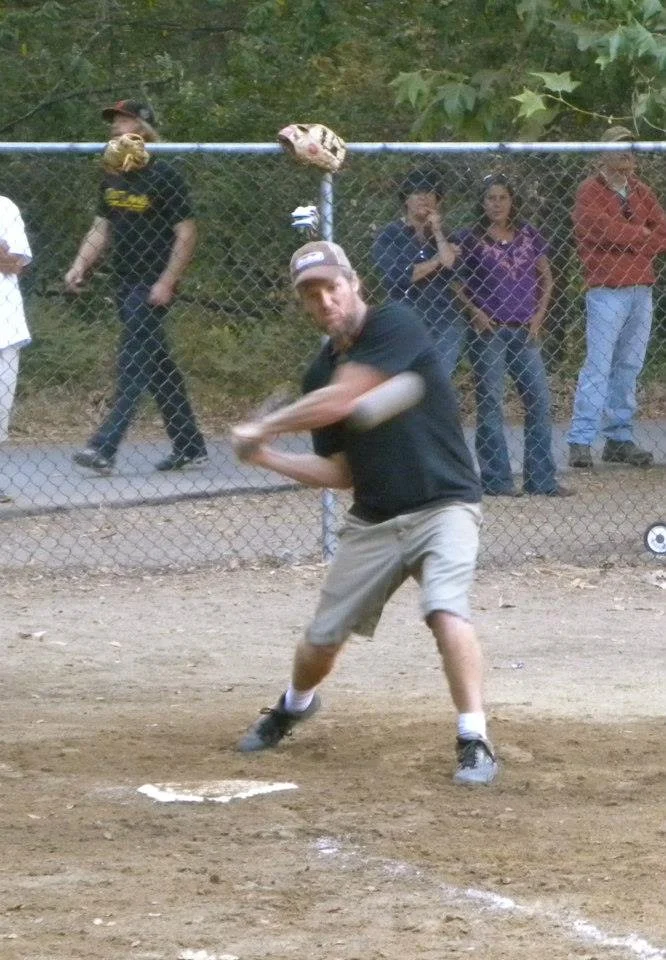 A man in a black shirt and beige shorts batting at a baseball game.