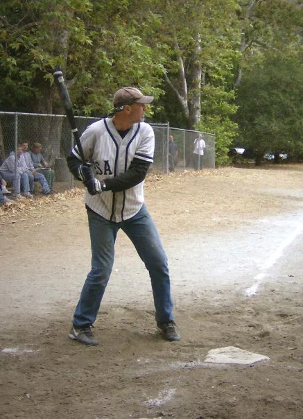 A person wearing a baseball jersey and cap, holding a bat, standing at home plate on a baseball field, preparing to bat.