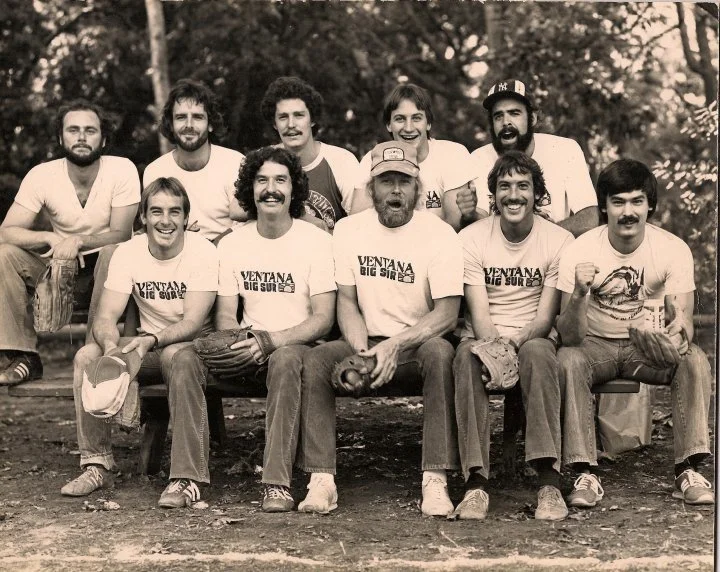Group of ten men sitting and standing outdoors, smiling, with some wearing baseball caps and t-shirts with "Ventana Big Sur" text.