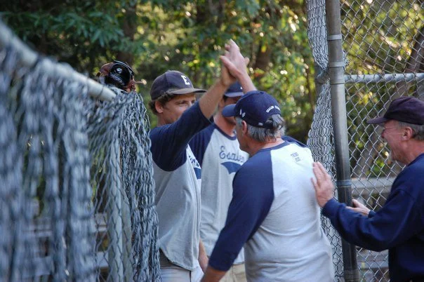 Baseball players and coach celebrating in dugout, high-fiving