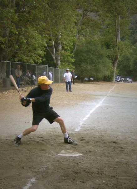 Child in yellow hat swings a baseball bat at a ball on a dirt baseball field.