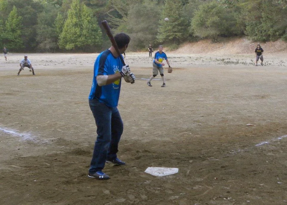 Person preparing to hit a baseball at a baseball field with other players in the background.