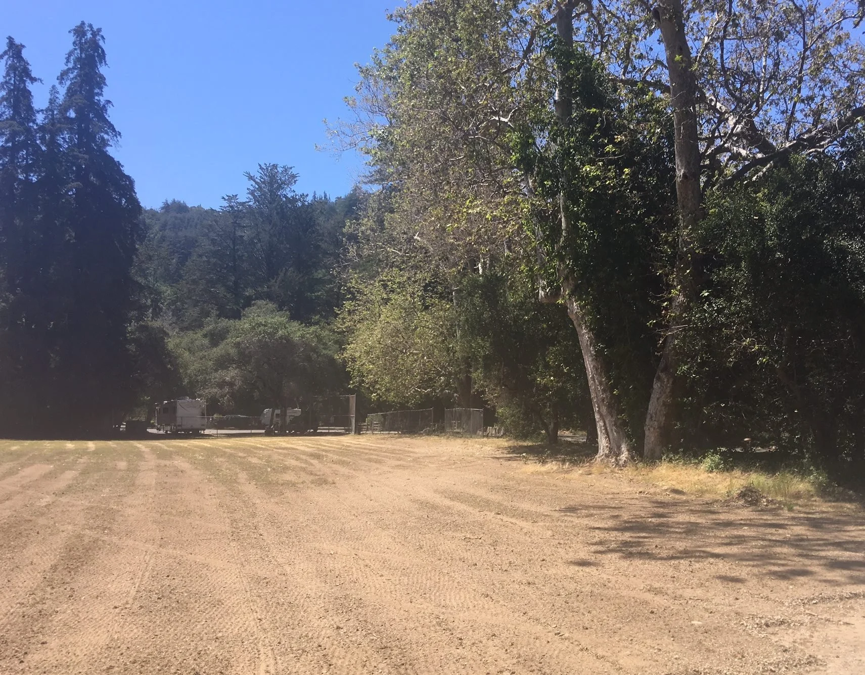 A dirt parking lot with several trees and a few rv campers in the background, under a clear blue sky.