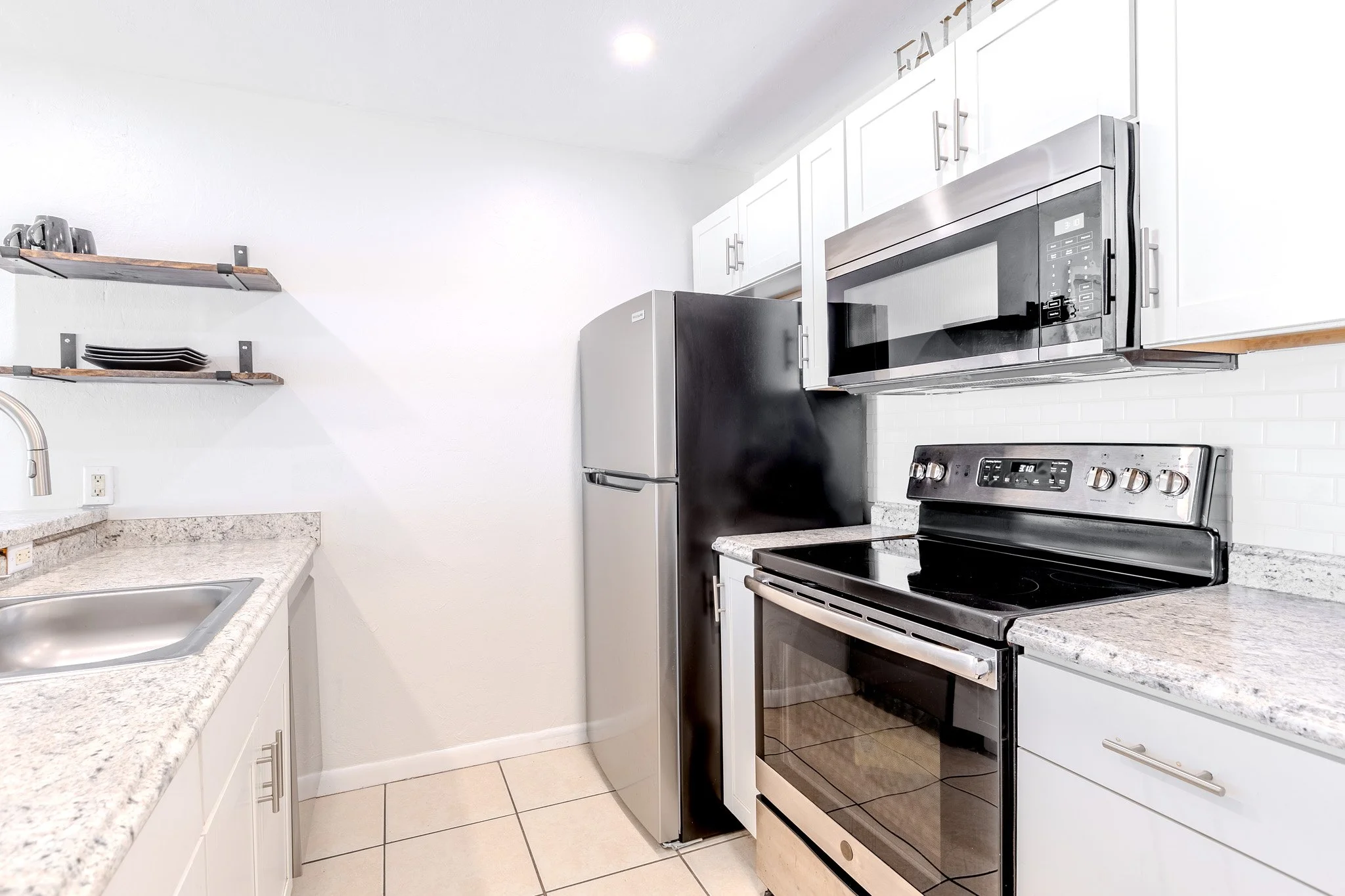 Modern kitchen with white cabinets, stainless steel appliances including a microwave, refrigerator, and oven. Granite countertops and tiled floor.