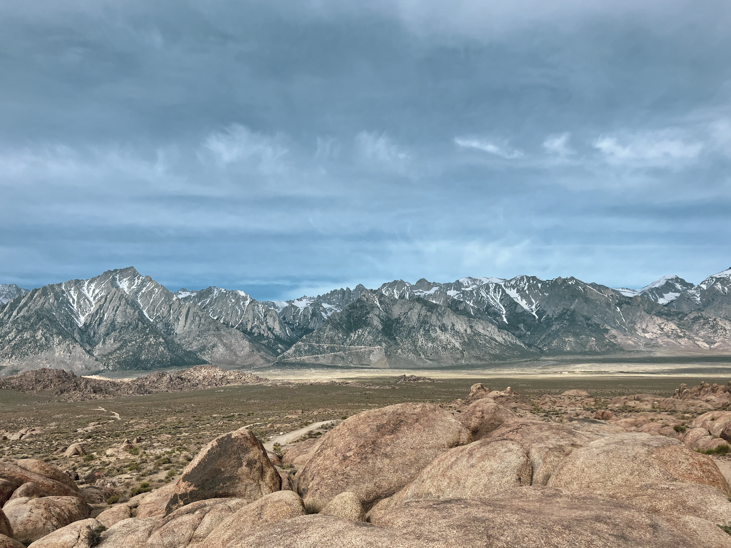 Snow-capped mountains under a partly cloudy sky with rocky terrain and scattered boulders in the foreground.
