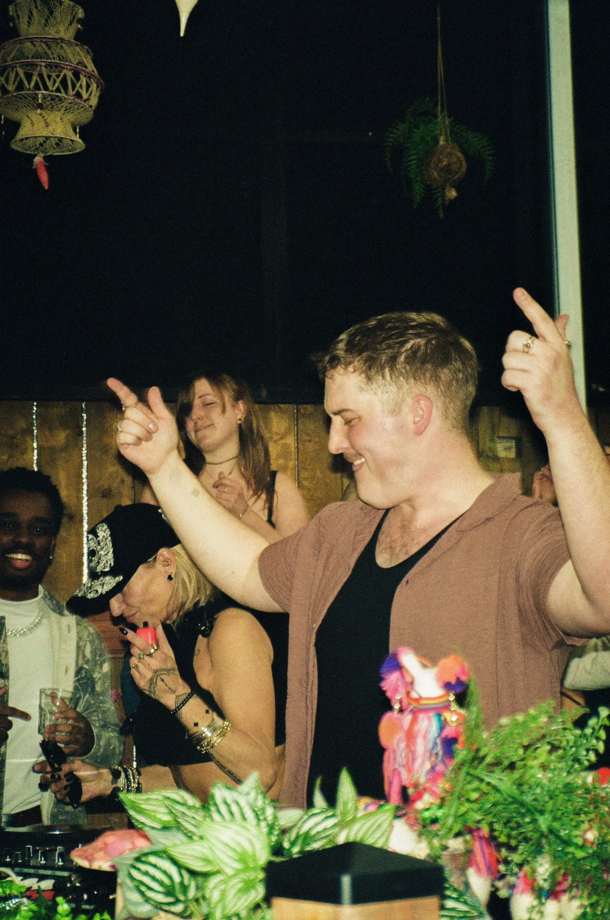 People dancing and socializing at a party with plants and decorations in the foreground.