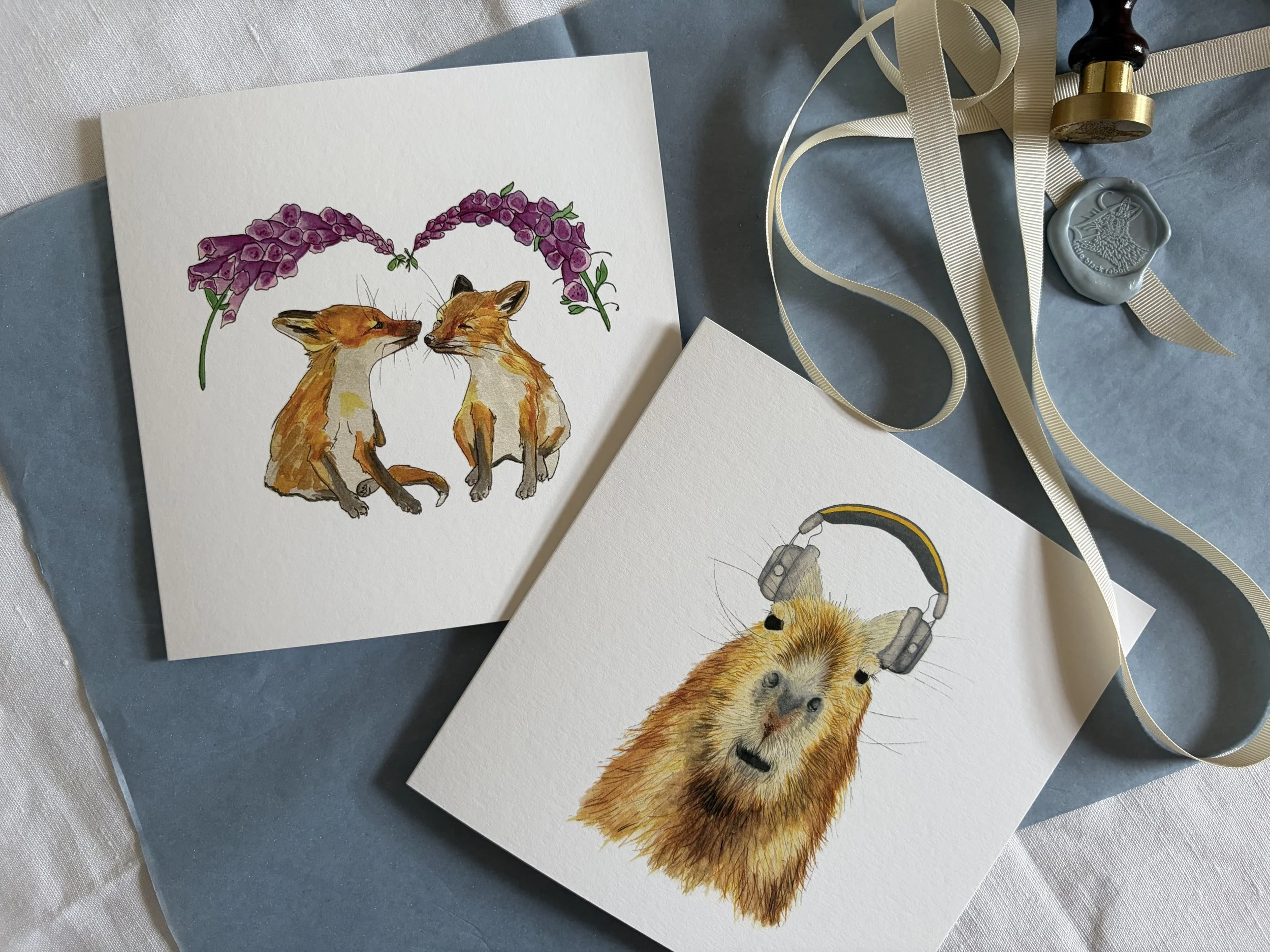 Watercolor illustrations of animals, including two foxes and a guinea pig with headphones, decorated with purple flowers and beige ribbons.