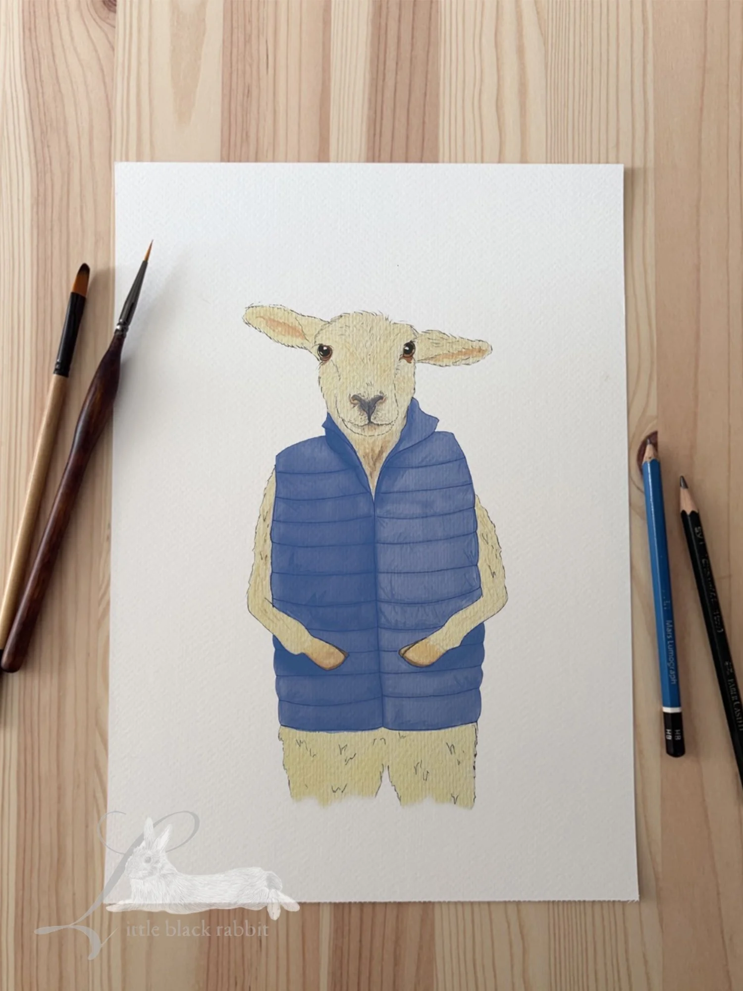 Original watercolour painting of a sheep in a blue quilted gilet on a wooden table with pencils and paintbrushes.
