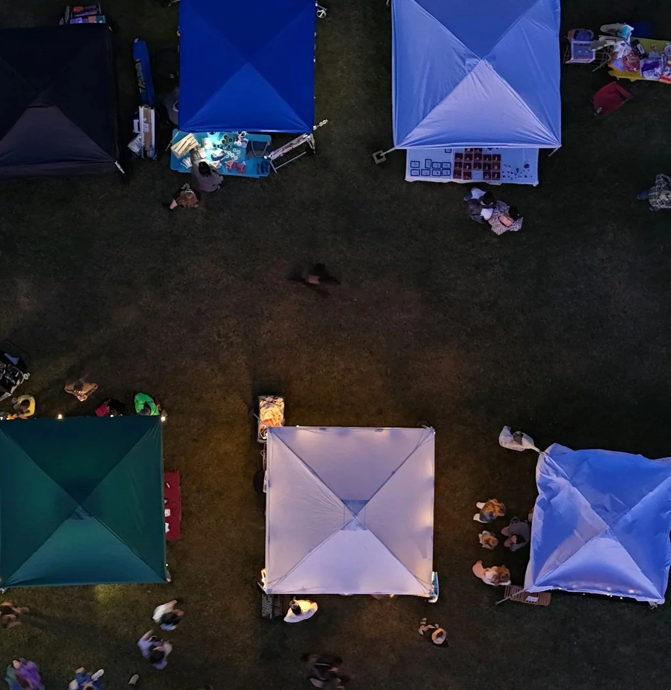 Overhead view of a nighttime outdoor market with several tents and people walking around.