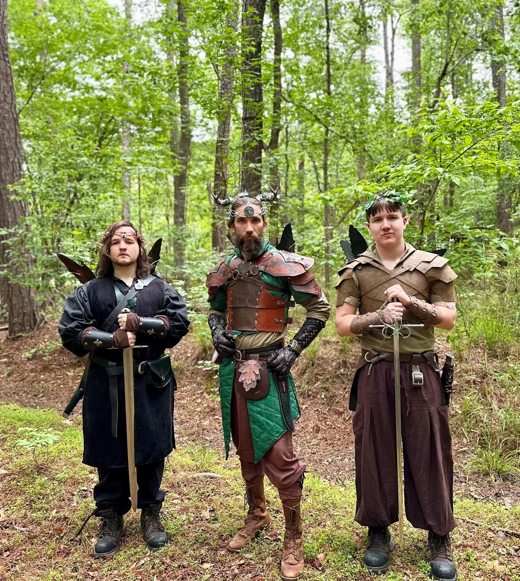 Three young men dressed as fantasy characters standing in a green forest.