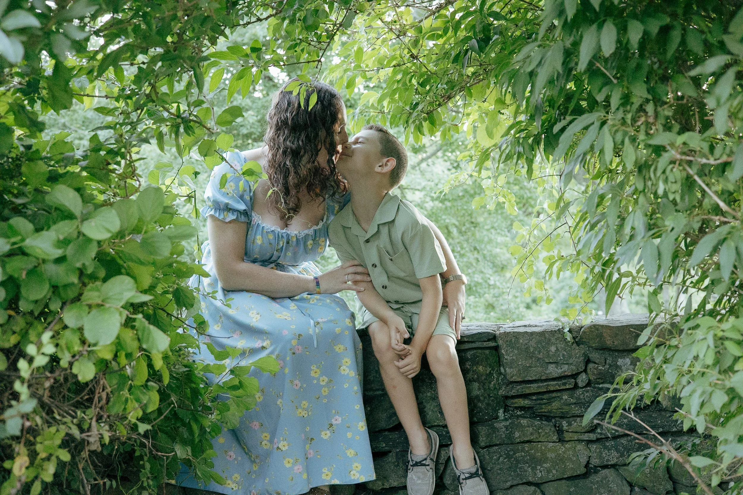 Mother and son sitting on a rock wall in an alcove of foliage