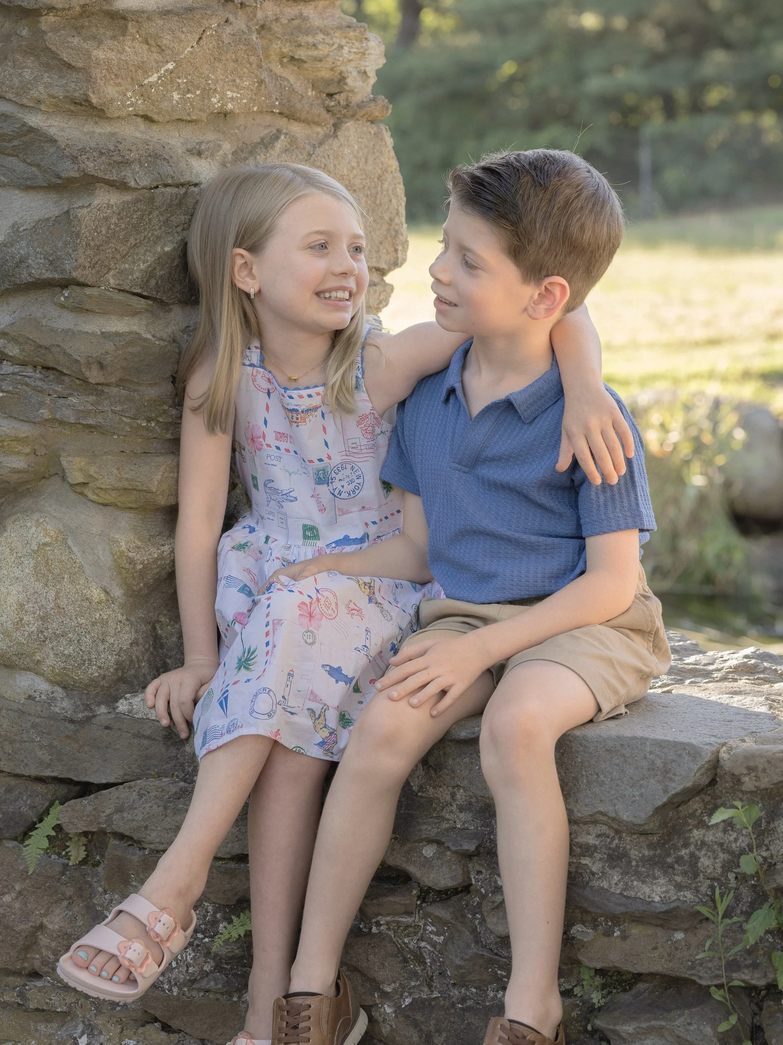Brother and sister sitting on a rock wall in a park