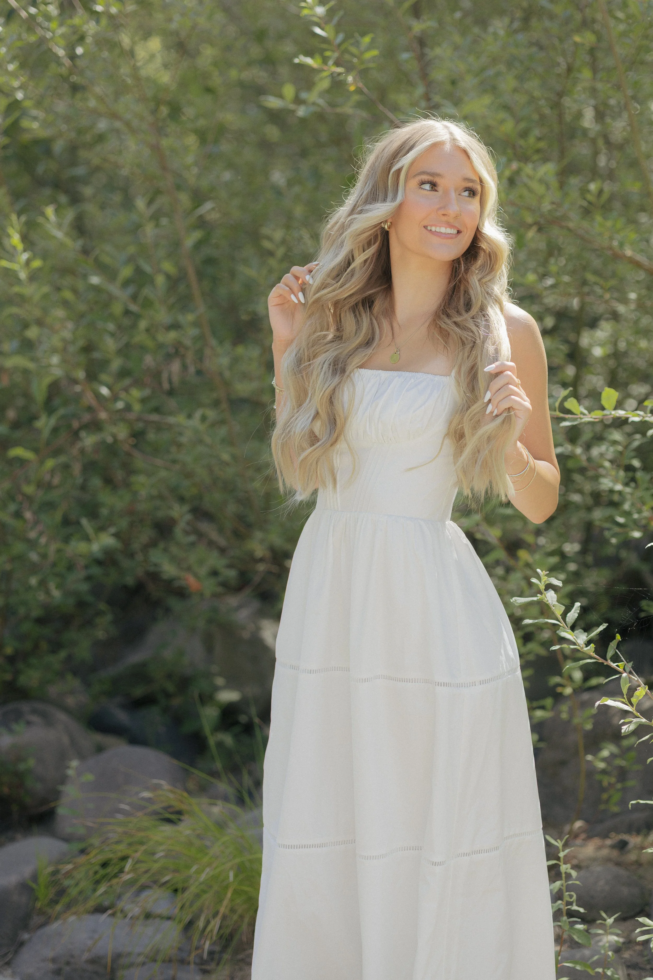 Blonde high school senior in white dress getting pictures in front of grenery