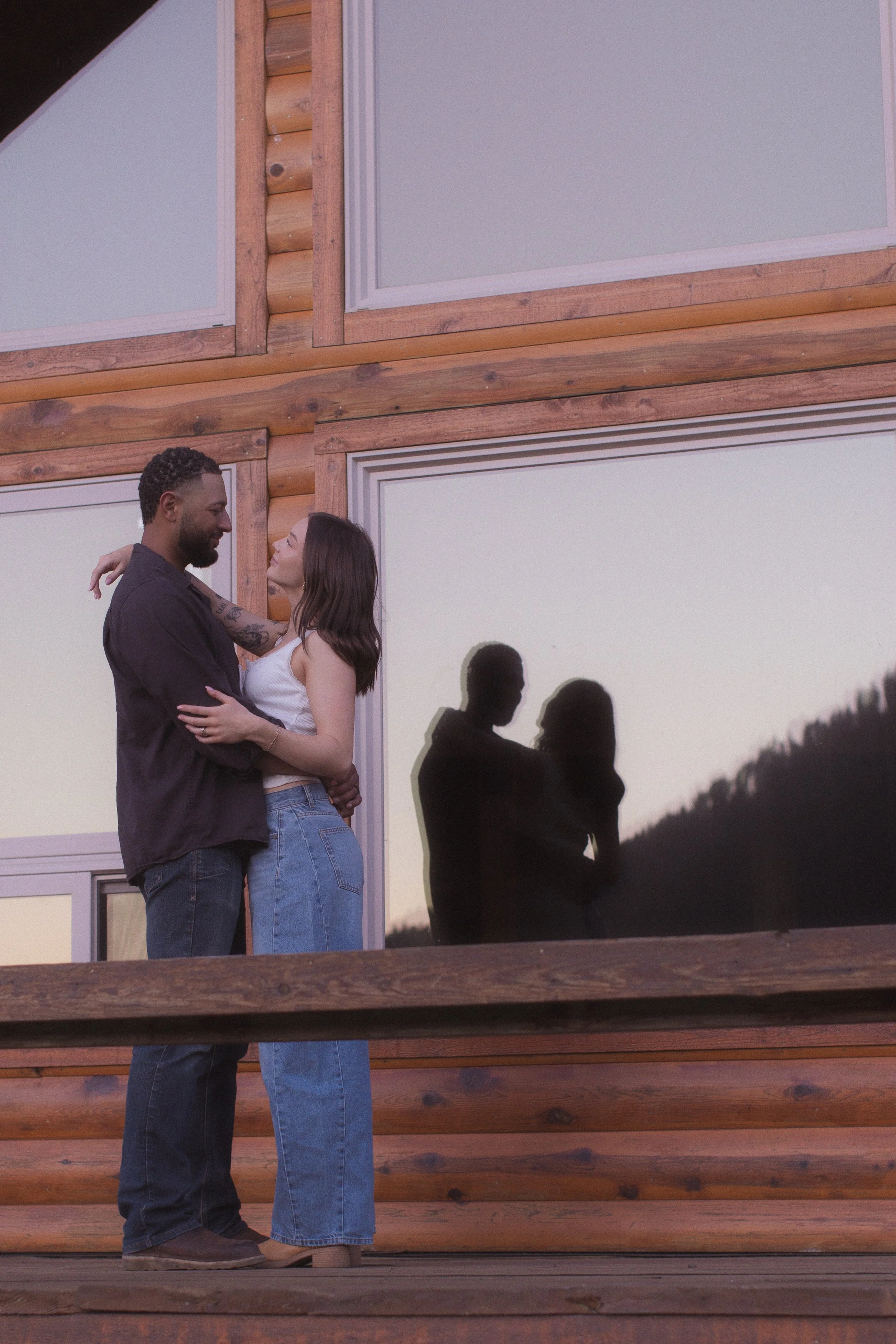 Man and woman in an embrace with their reflection in the log cabin window. 