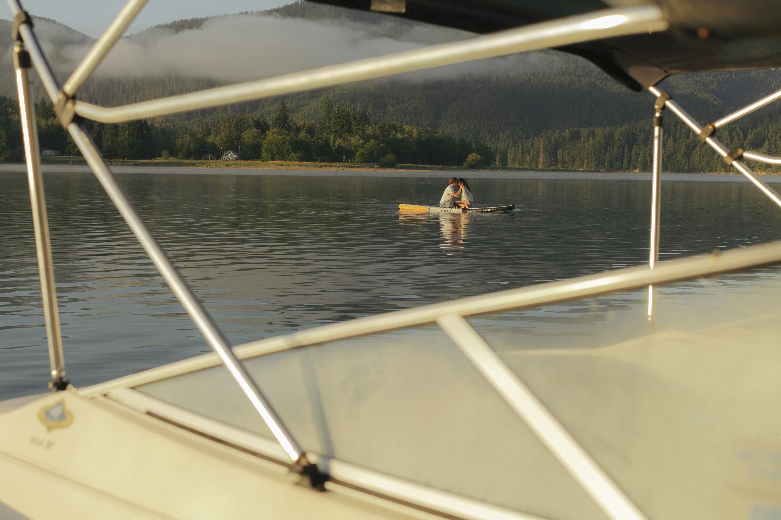 Man and woman on the lake on a paddle board shot through the view of a boat