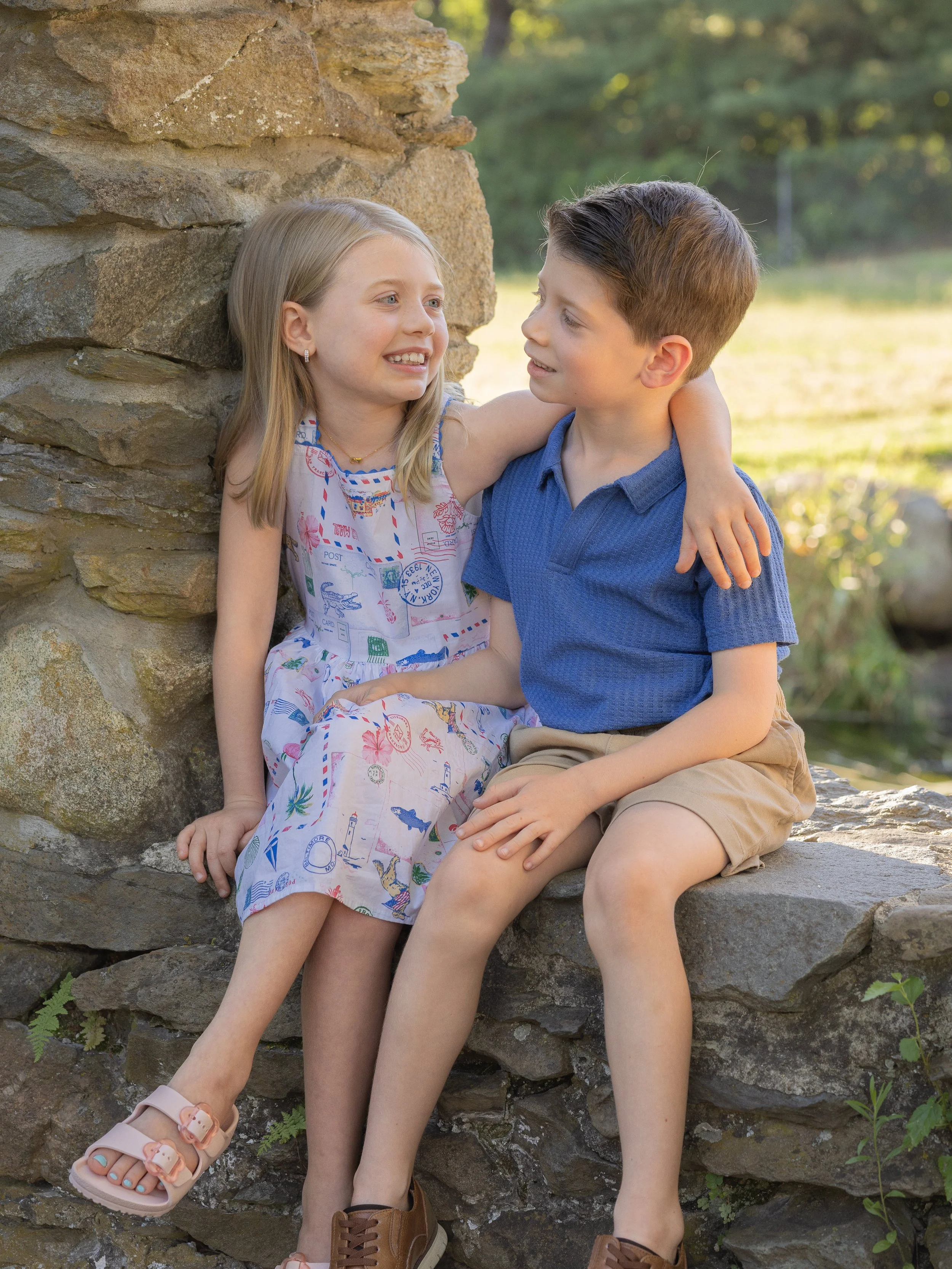Brother and sister sitting on a rock wall in a park