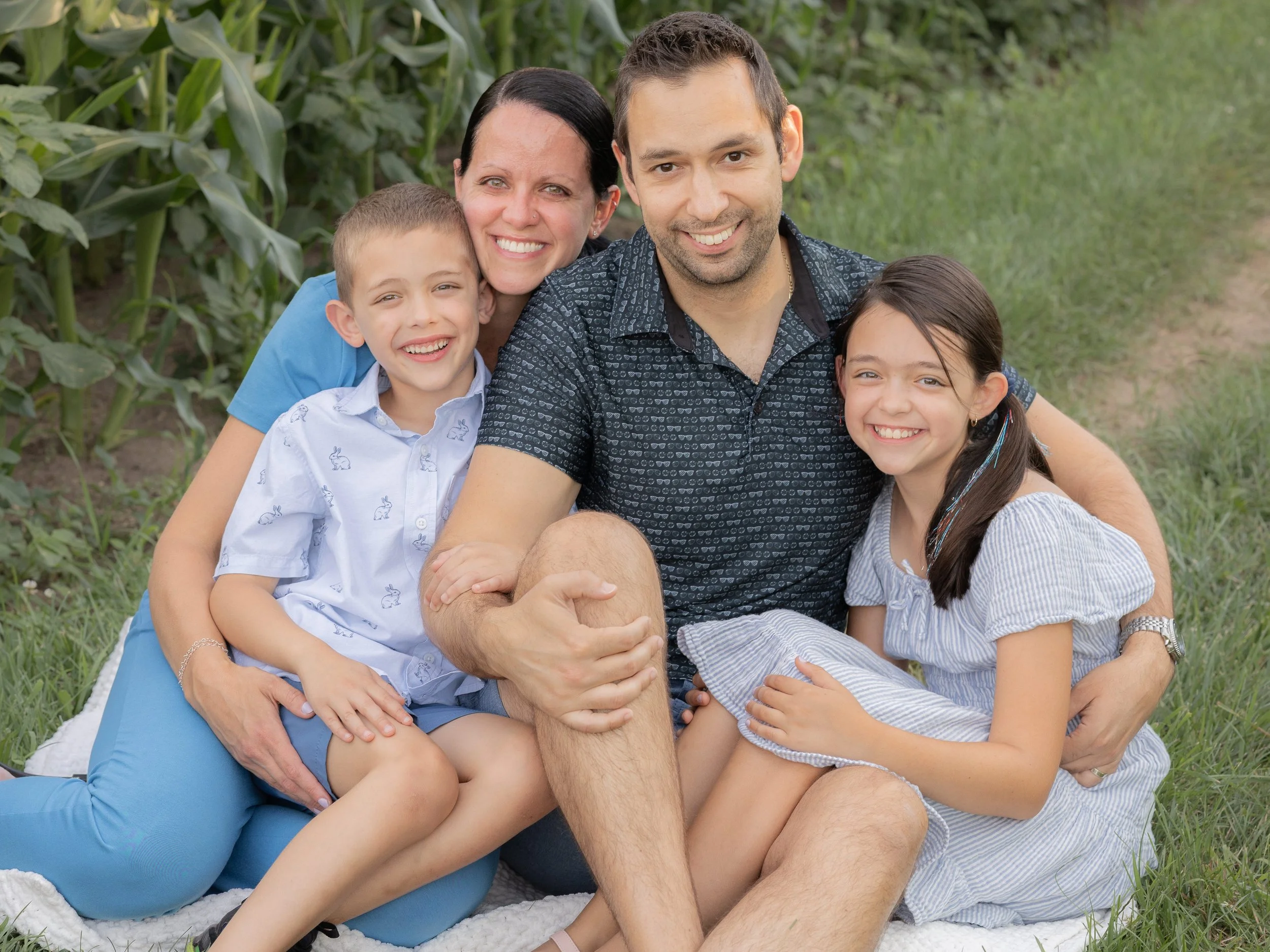 Family of four sitting in a corn field for family pictures in matching outfits