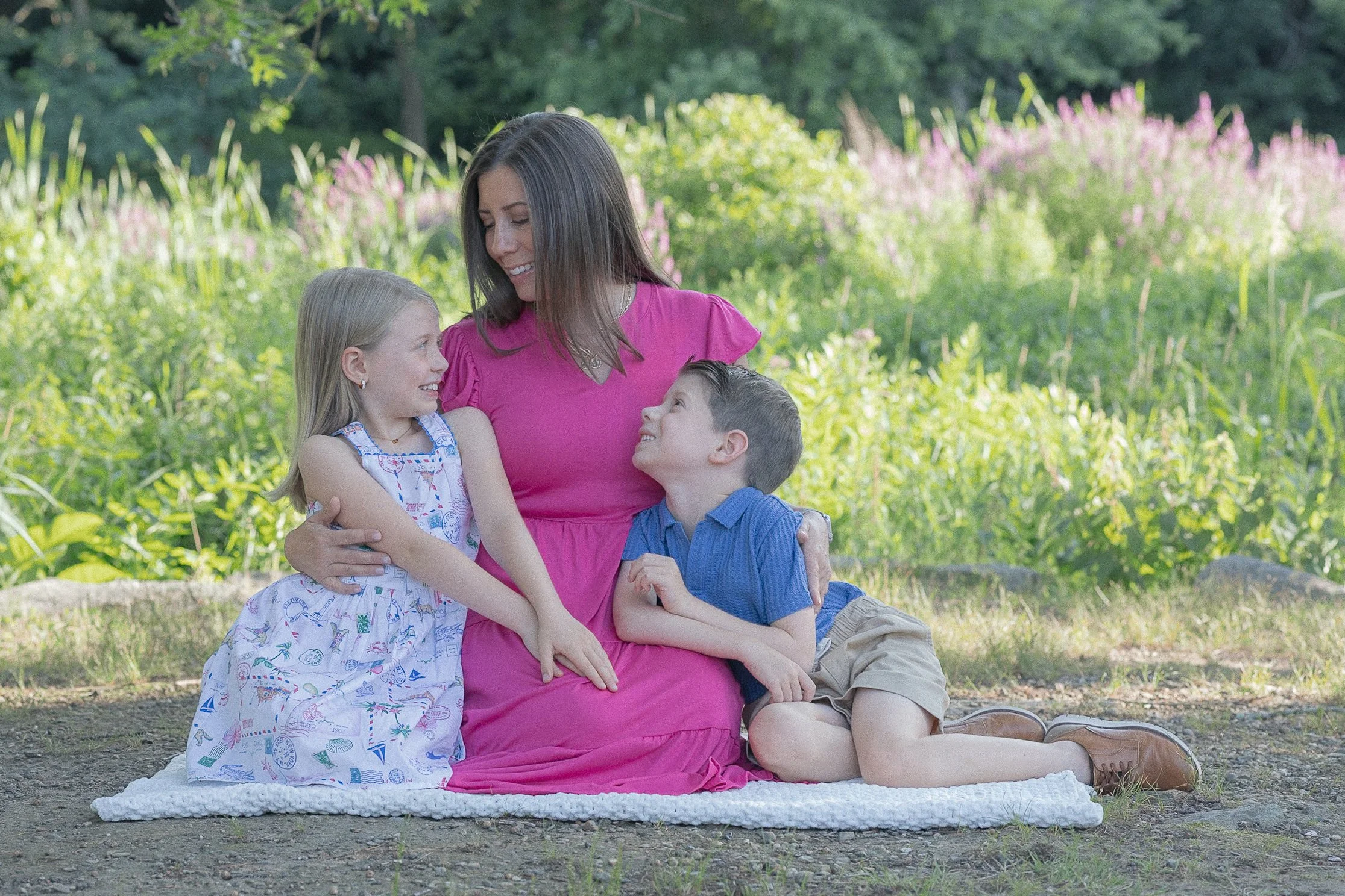 Mother in pink dress with two young kids in front of a flower field