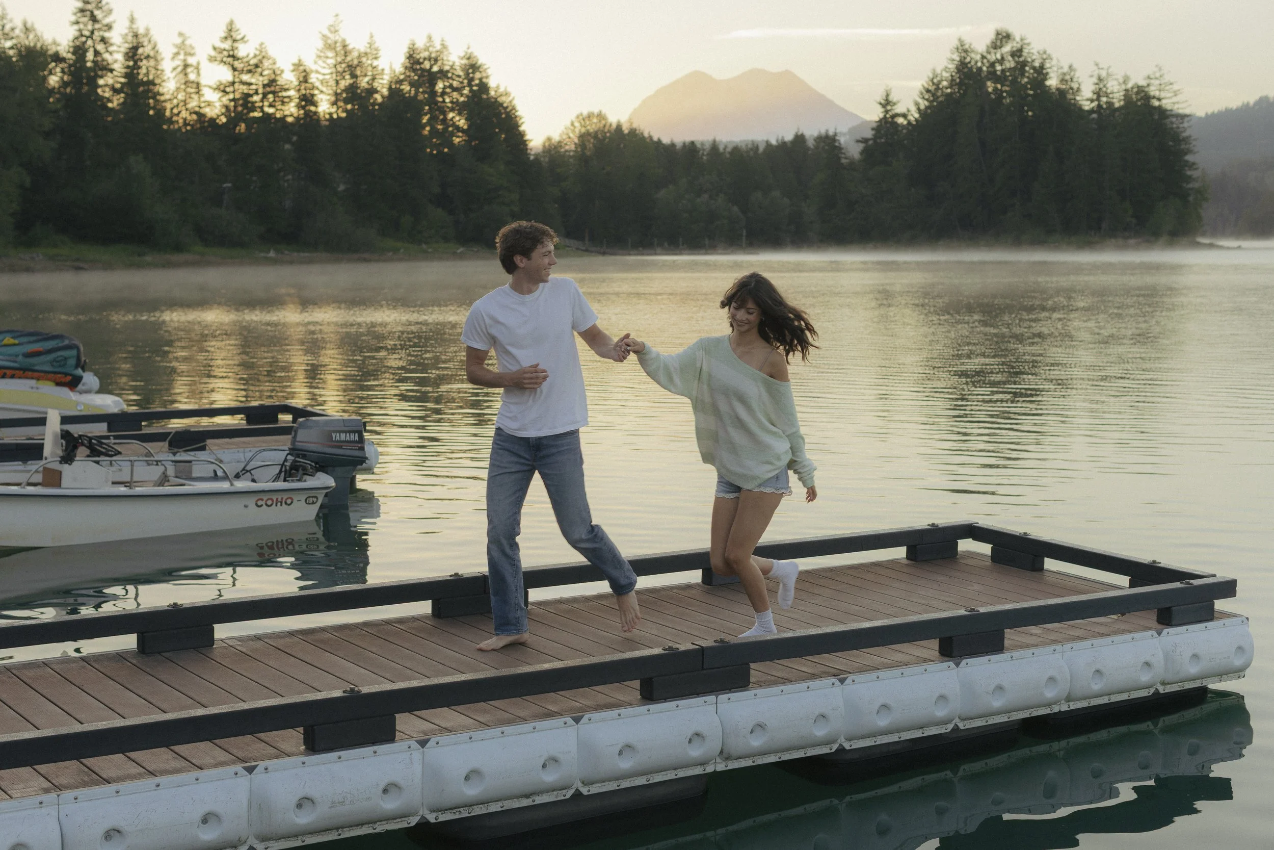 Man and woman holding hands and running across a dock on a lake at sunrise
