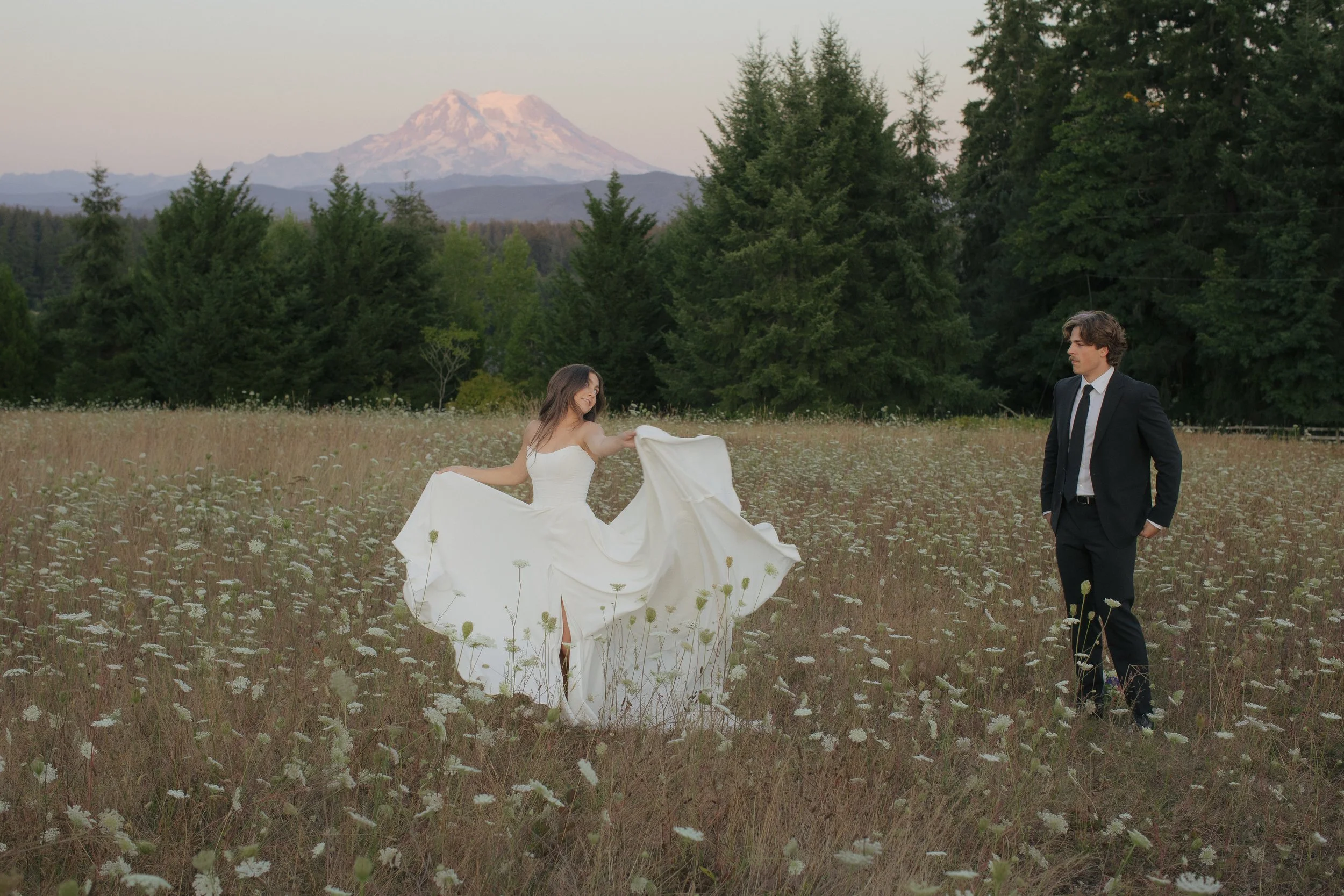 Woman in bridal gown dancing for her new husband in front of Mt. Rainier Washington. Flower field and pink mountain. 