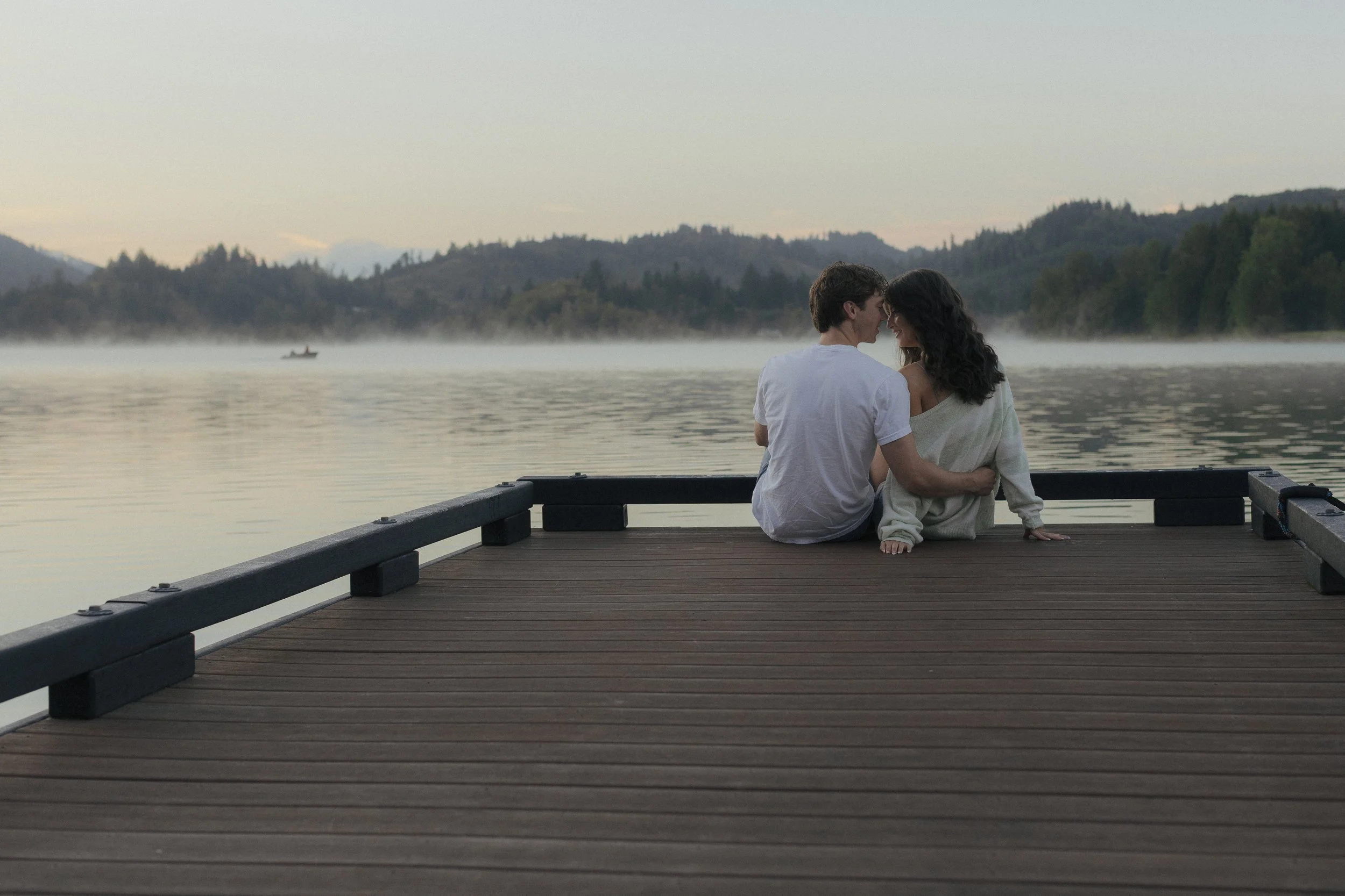 Man and woman sitting at the edge of a dock on a lake at sunrise