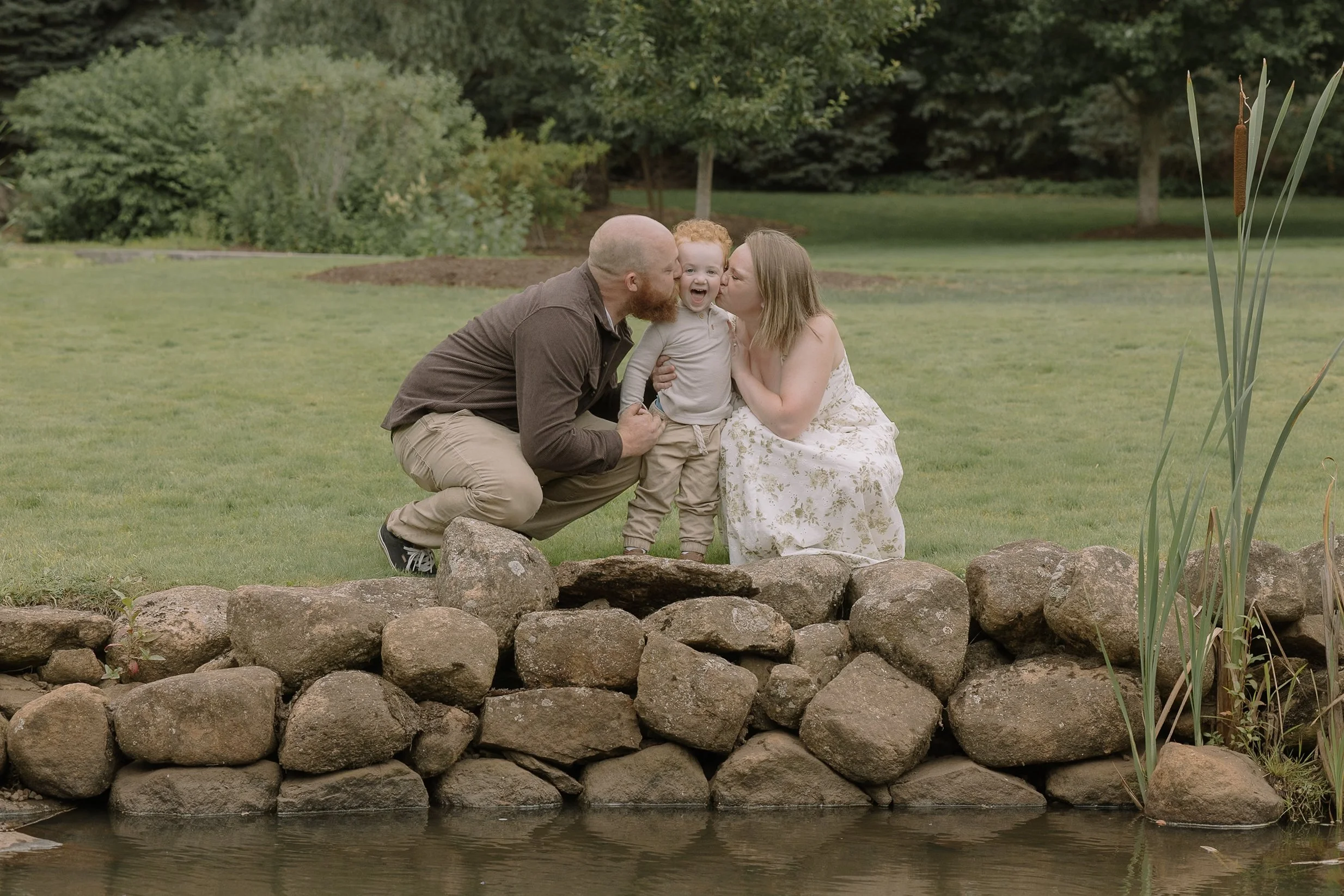Mom and dad with young red haired toddler boy in a grassy park
