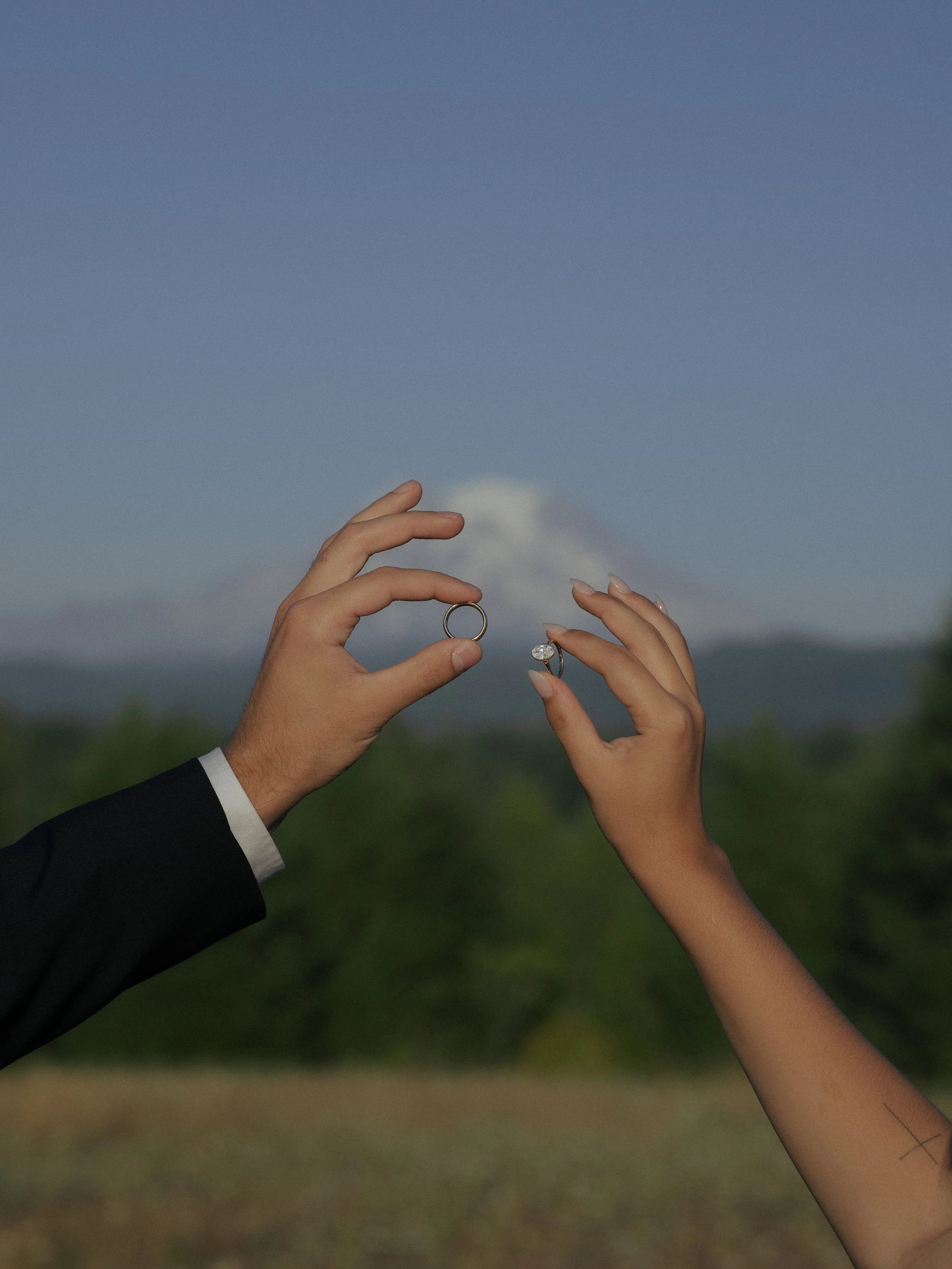 Newlyweds holding up their wedding rings in front of Mt. Rainier in Washington. 