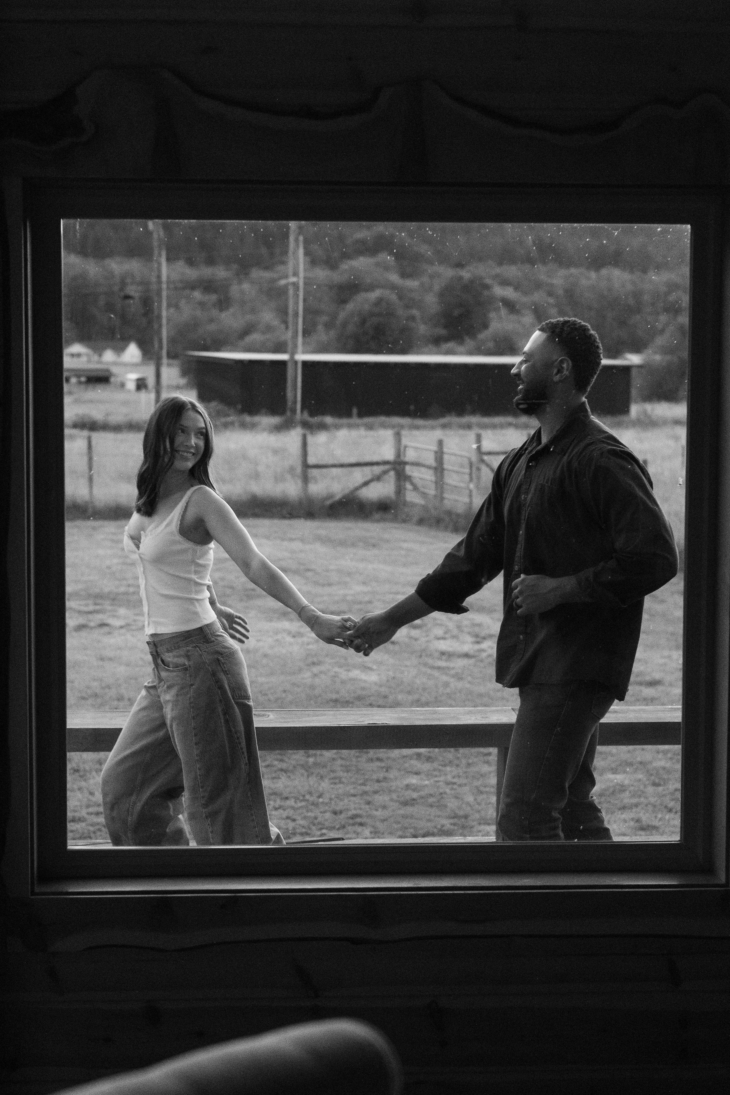 Woman leading man in front of a picture window in black and white. 