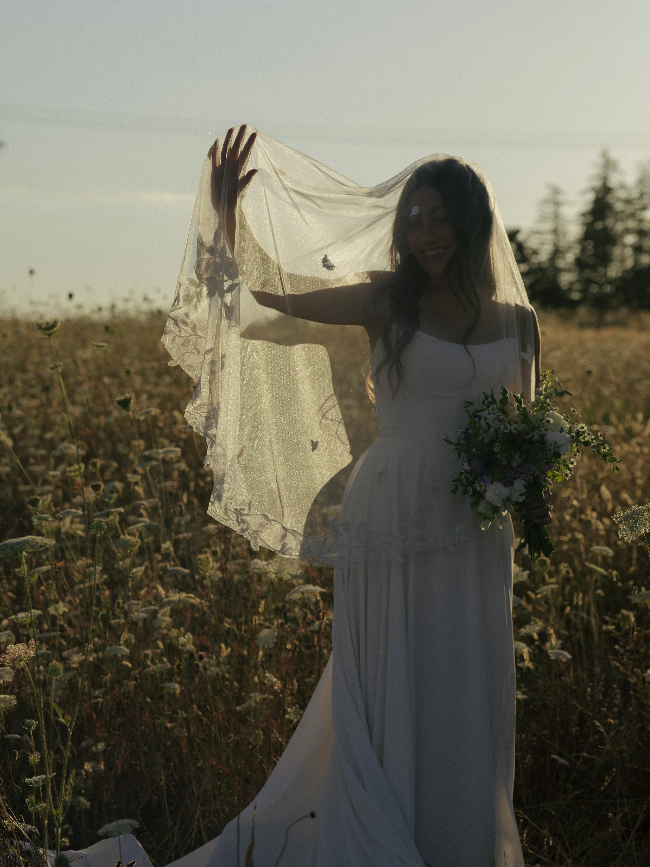 Woman in a bridal gown with a veil over her face in a field of flowers. 